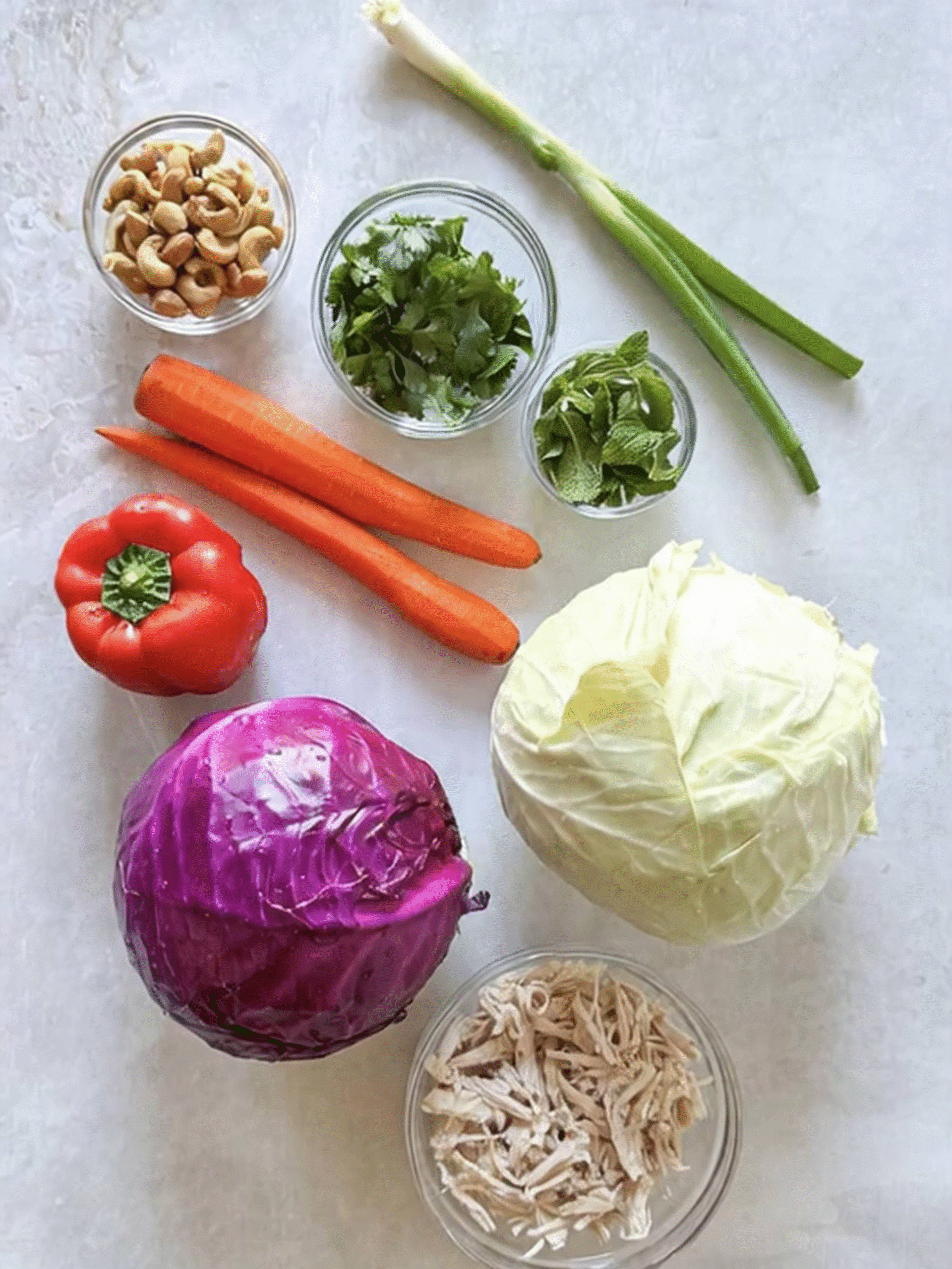 Asian Crunchy Salad Ingredients Flat Lay Fresh ingredients for Asian Crunchy Salad including red cabbage, green cabbage, carrots, bell pepper, herbs, shredded chicken, and cashews