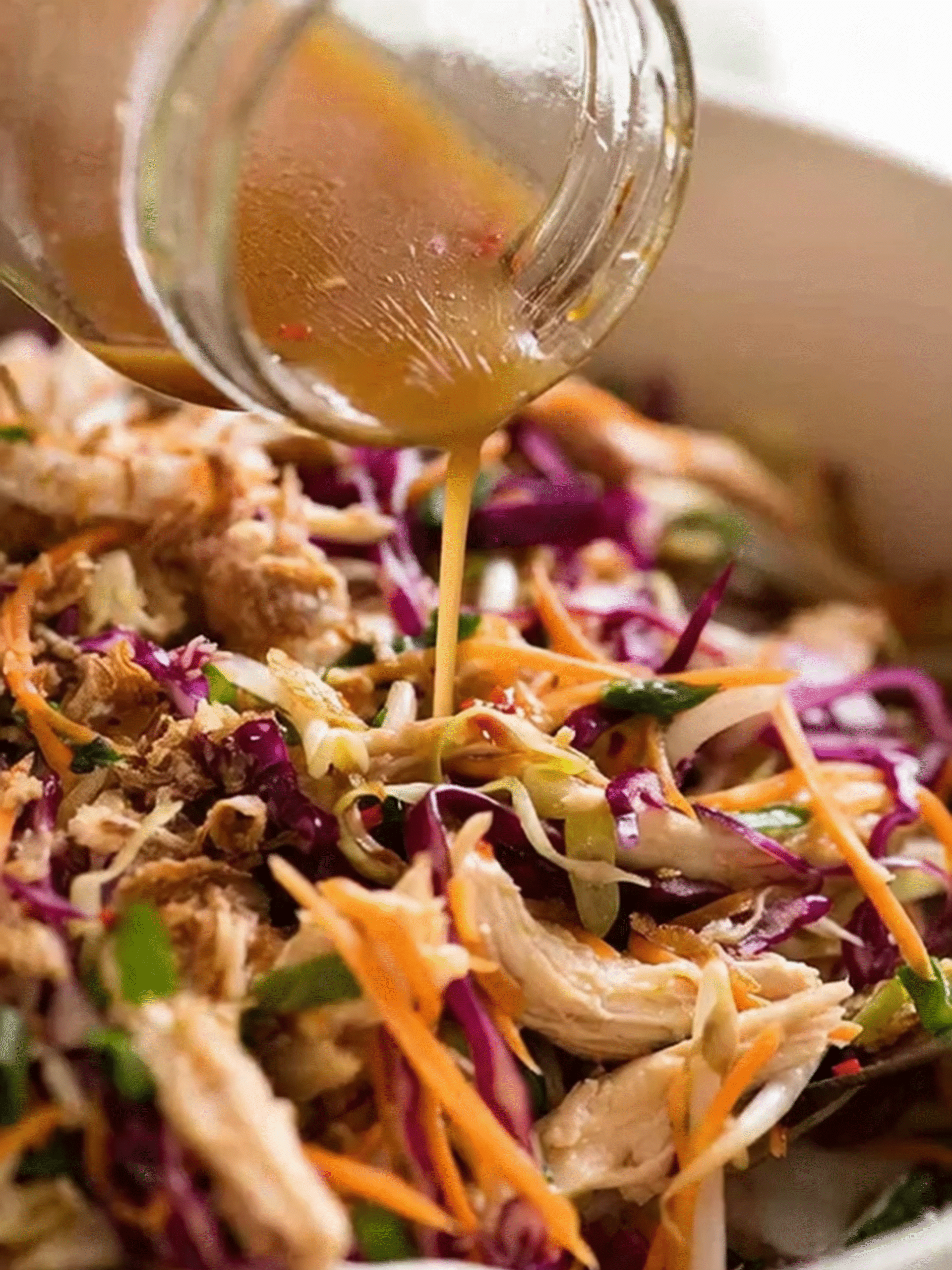 Dressing Asian Crunchy Salad with Sesame Ginger Sauce Pouring sesame ginger dressing over Asian Crunchy Salad with shredded chicken, cabbage, and carrots