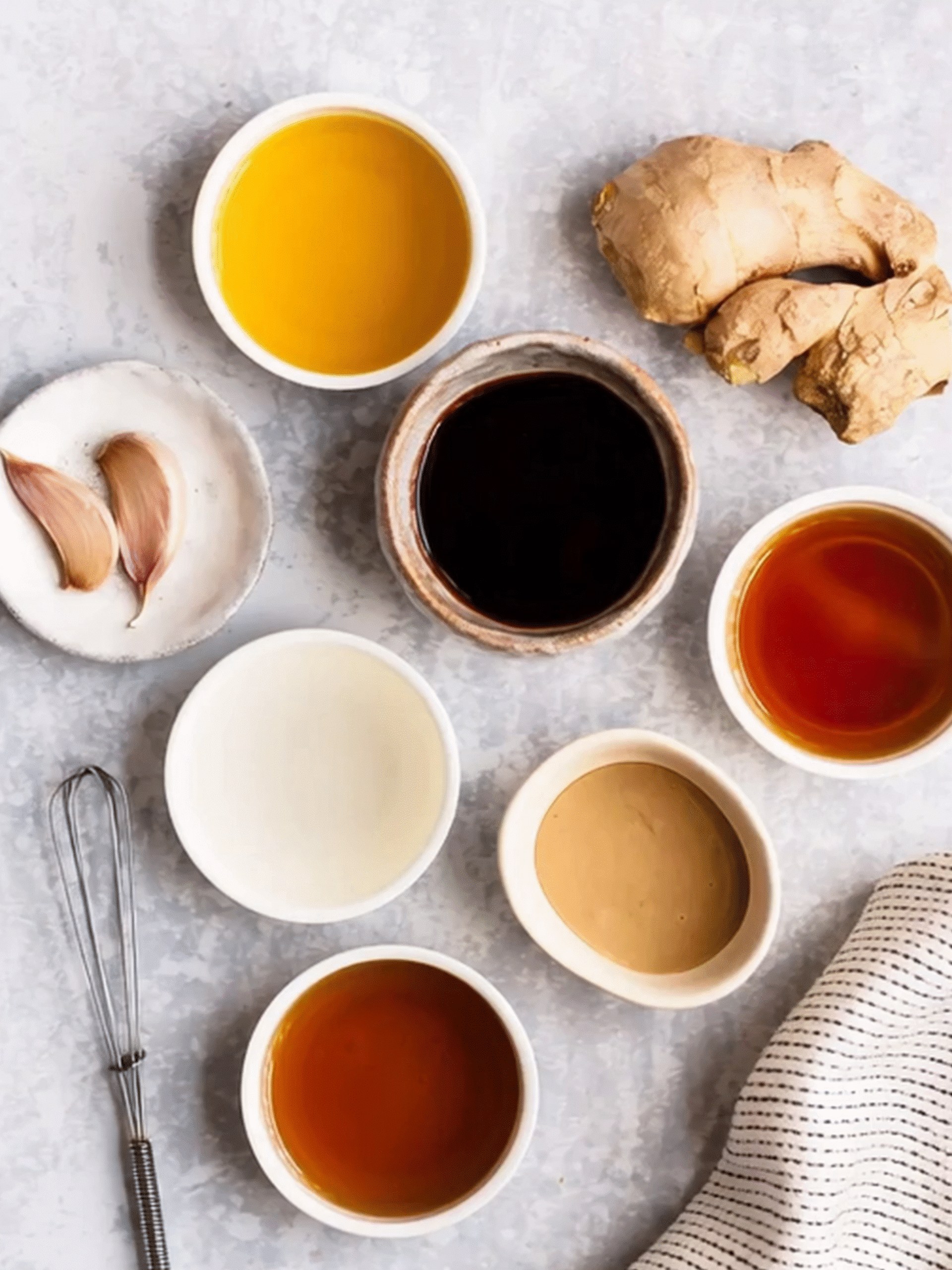 Ingredients for sesame ginger dressing including soy sauce, olive oil, garlic, ginger, tahini, rice vinegar, and honey in small bowls