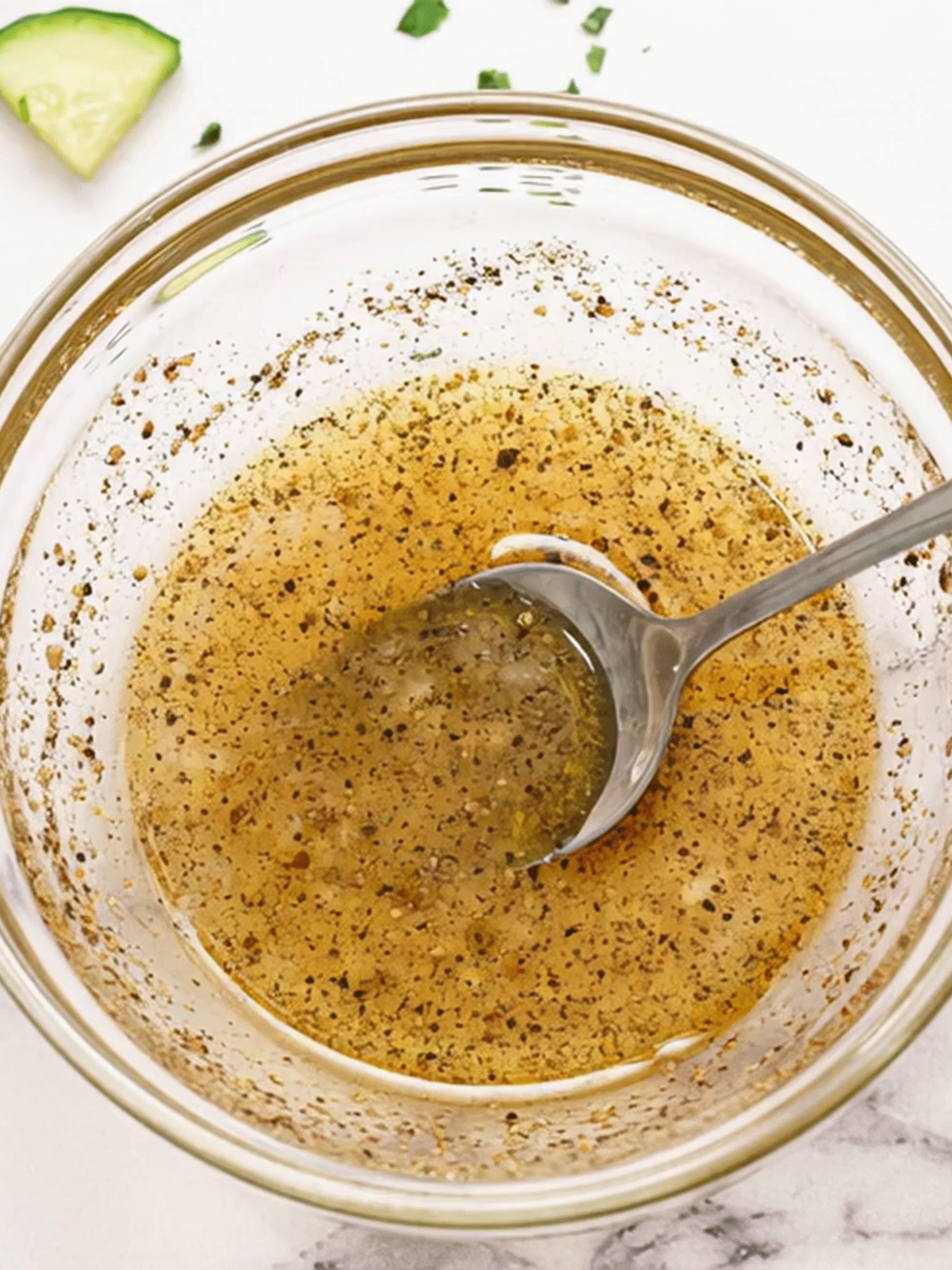 Fresh Lemon Vinaigrette for Tomato Cucumber Avocado Salad Homemade lemon vinaigrette dressing with black pepper and garlic in a glass bowl with a spoon