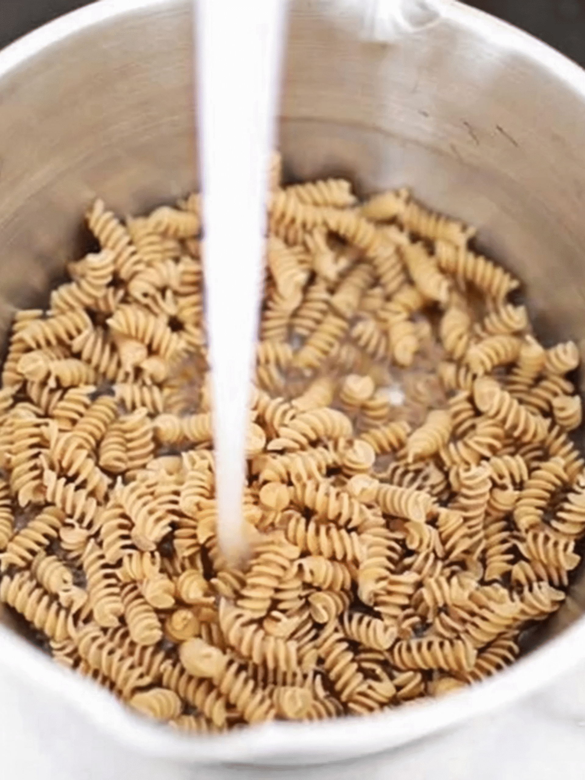 Rinsing Rotini Pasta for Creamy Summer Pasta Salad Rotini pasta being rinsed under cold water in a metal colander after cooking
