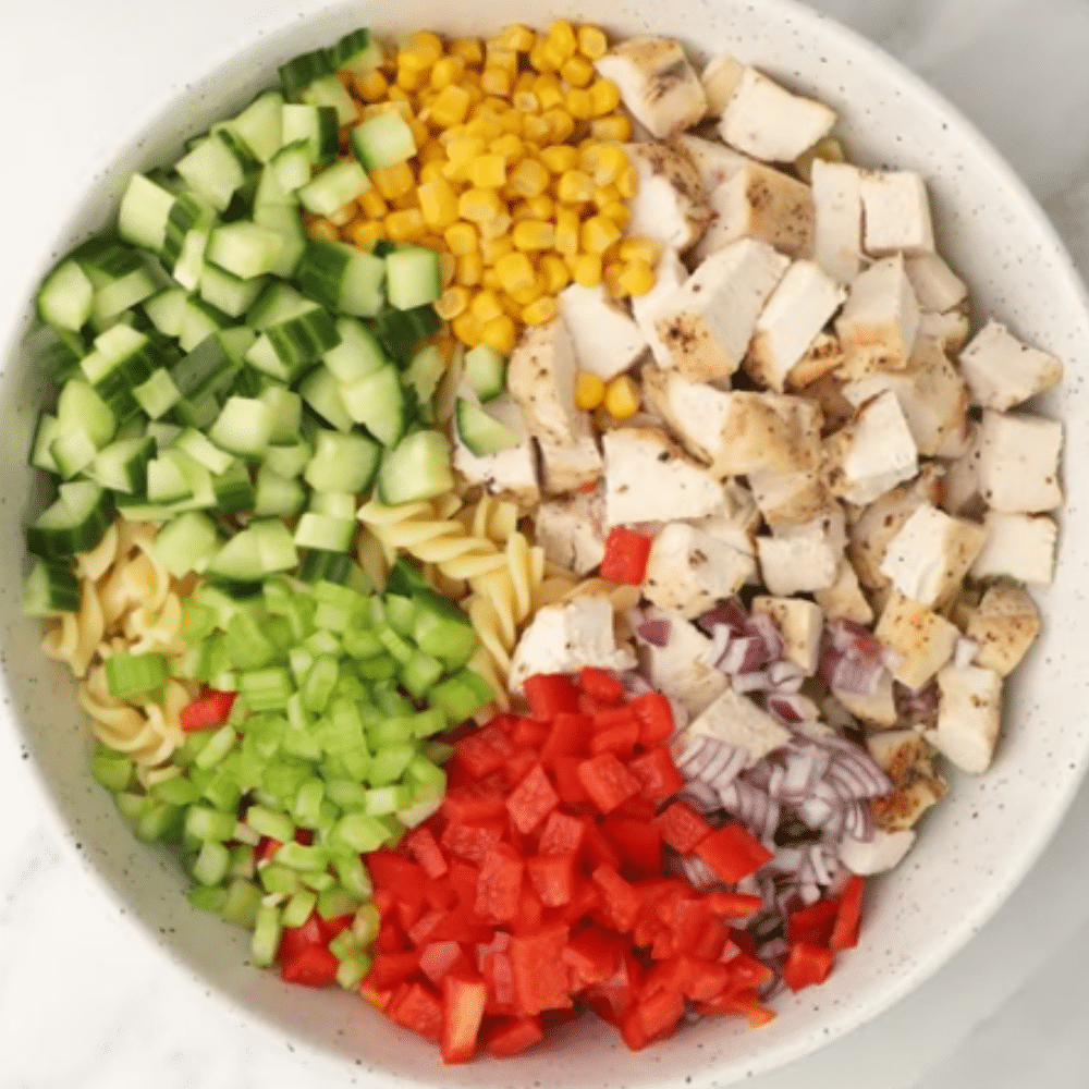 Chicken Ranch Pasta Salad Ingredients in Bowl Bowl filled with diced chicken, corn, cucumber, red bell pepper, celery, onion, and pasta ready to be mixed