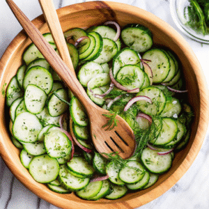 Fresh cucumber and red onion salad with dill in a wooden bowl with wooden serving utensils
