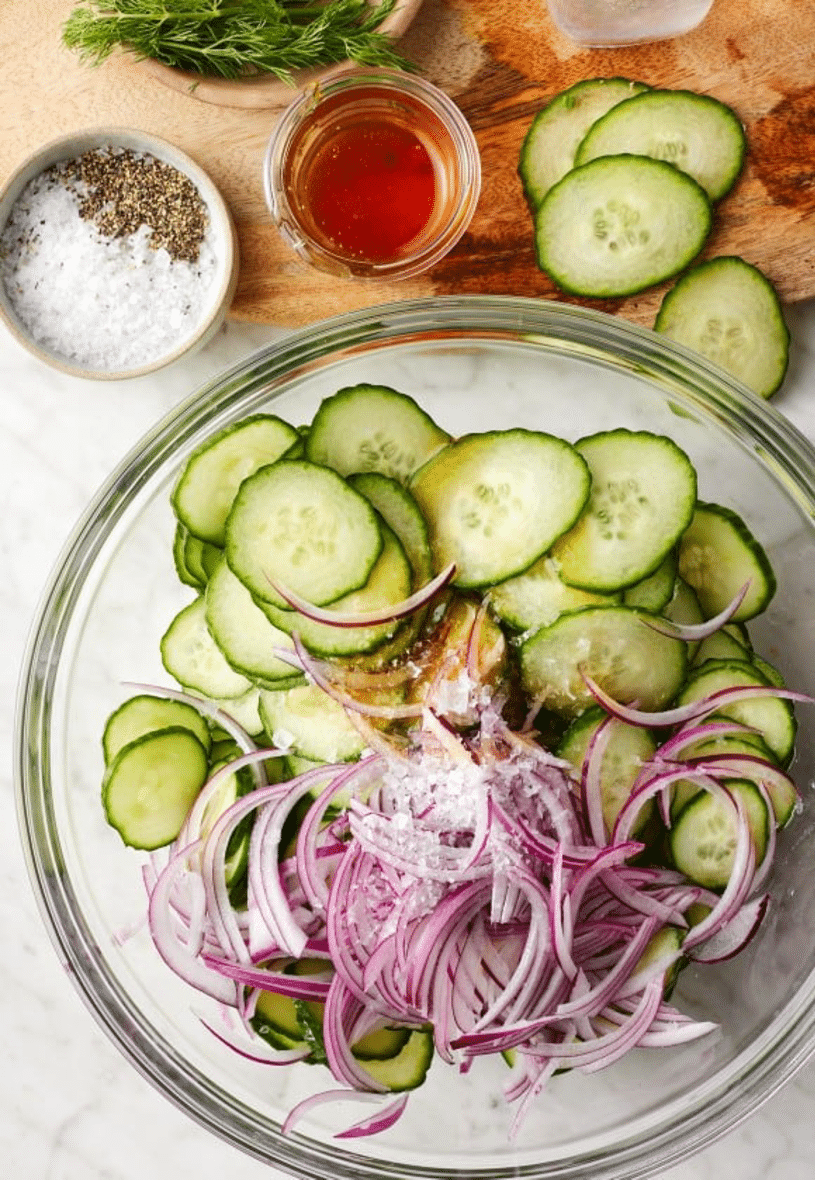 Cucumber and Red Onion Salad Preparation Glass bowl filled with sliced cucumbers and red onions with salt and vinegar, ready to make cucumber salad