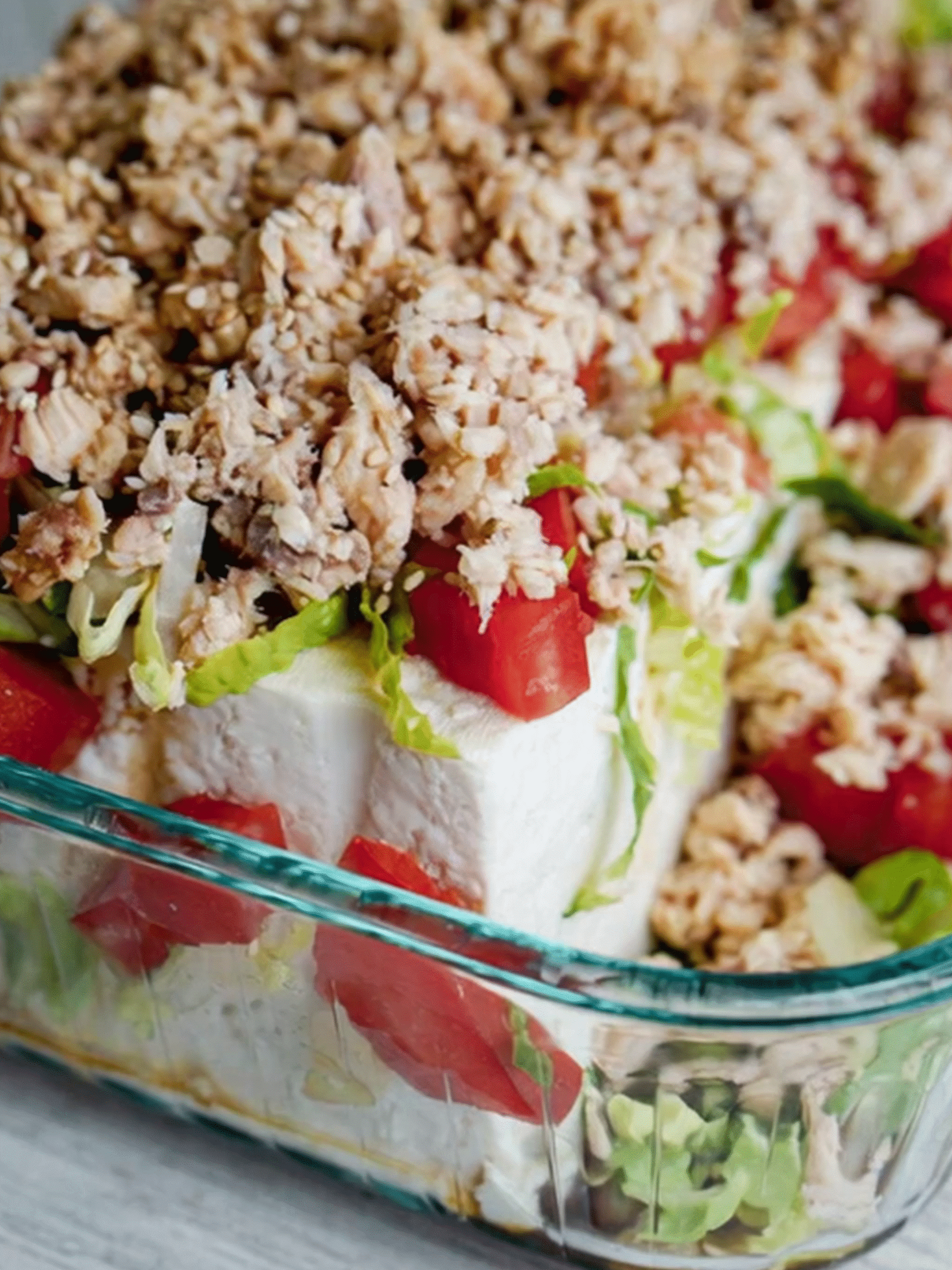 Cold tofu salad layered with shredded lettuce, diced tomatoes, and seasoned tuna in a glass dish