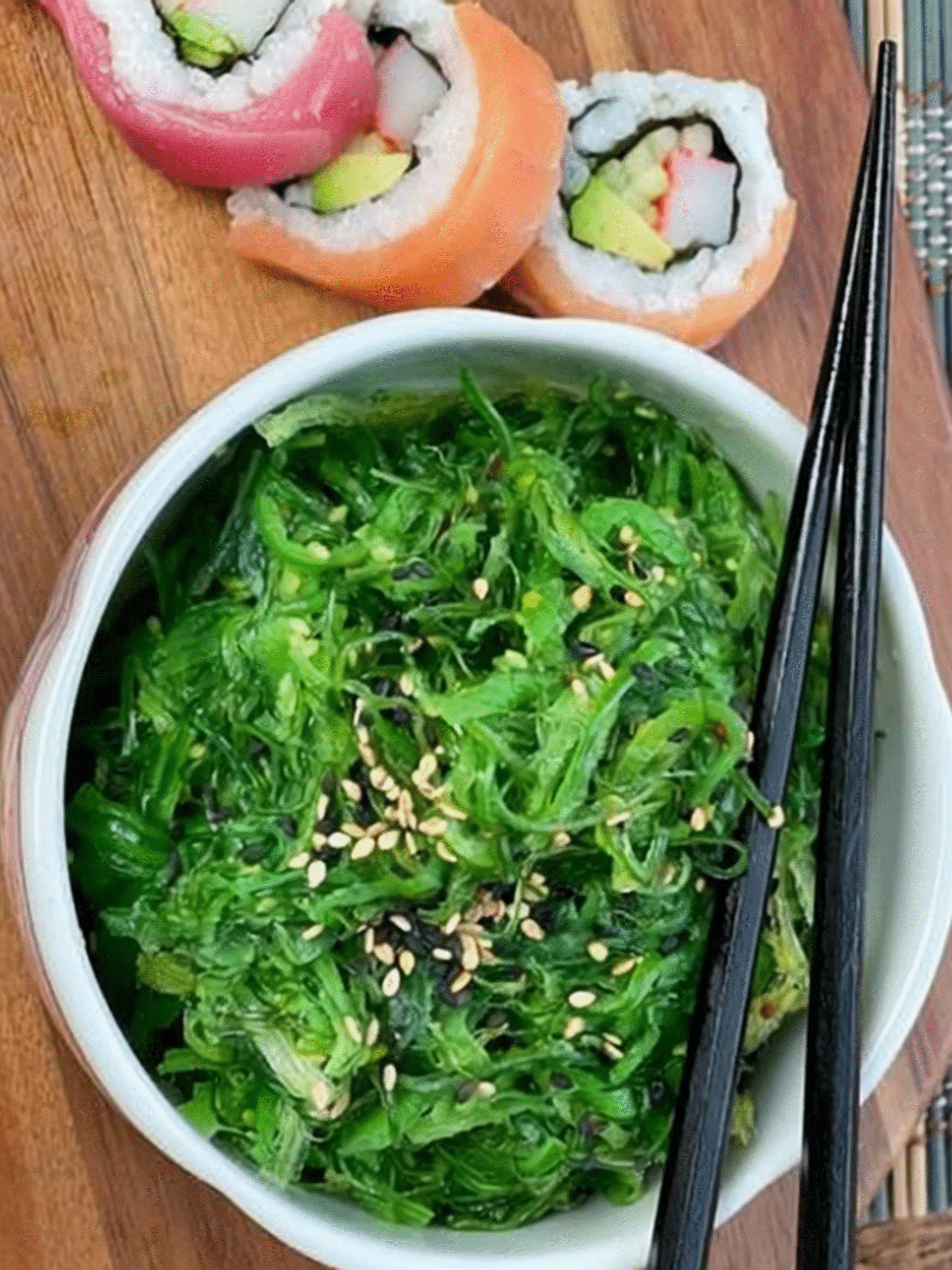 Japanese seaweed salad with sesame seeds served in a white bowl with sushi rolls on the side