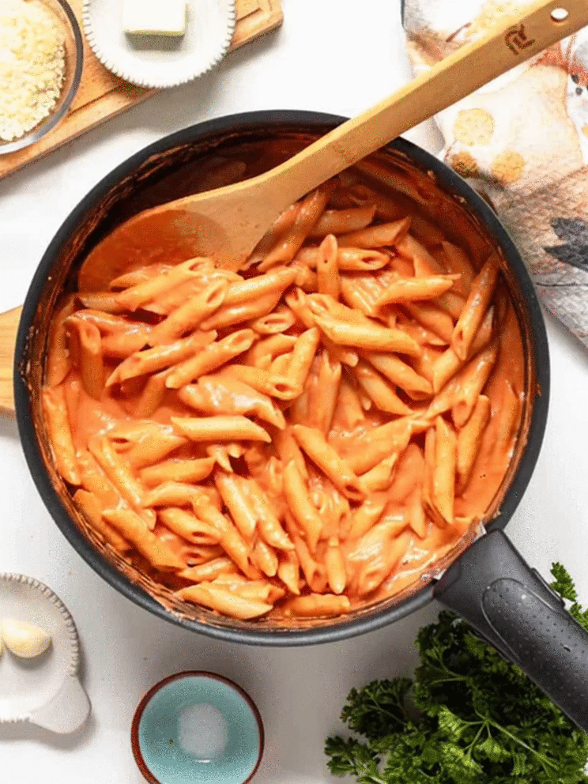 Penne Pasta Coated in Creamy Pink Salt Sauce Cooked penne pasta mixed with creamy pink salt tomato sauce in a non-stick pan with a wooden spoon