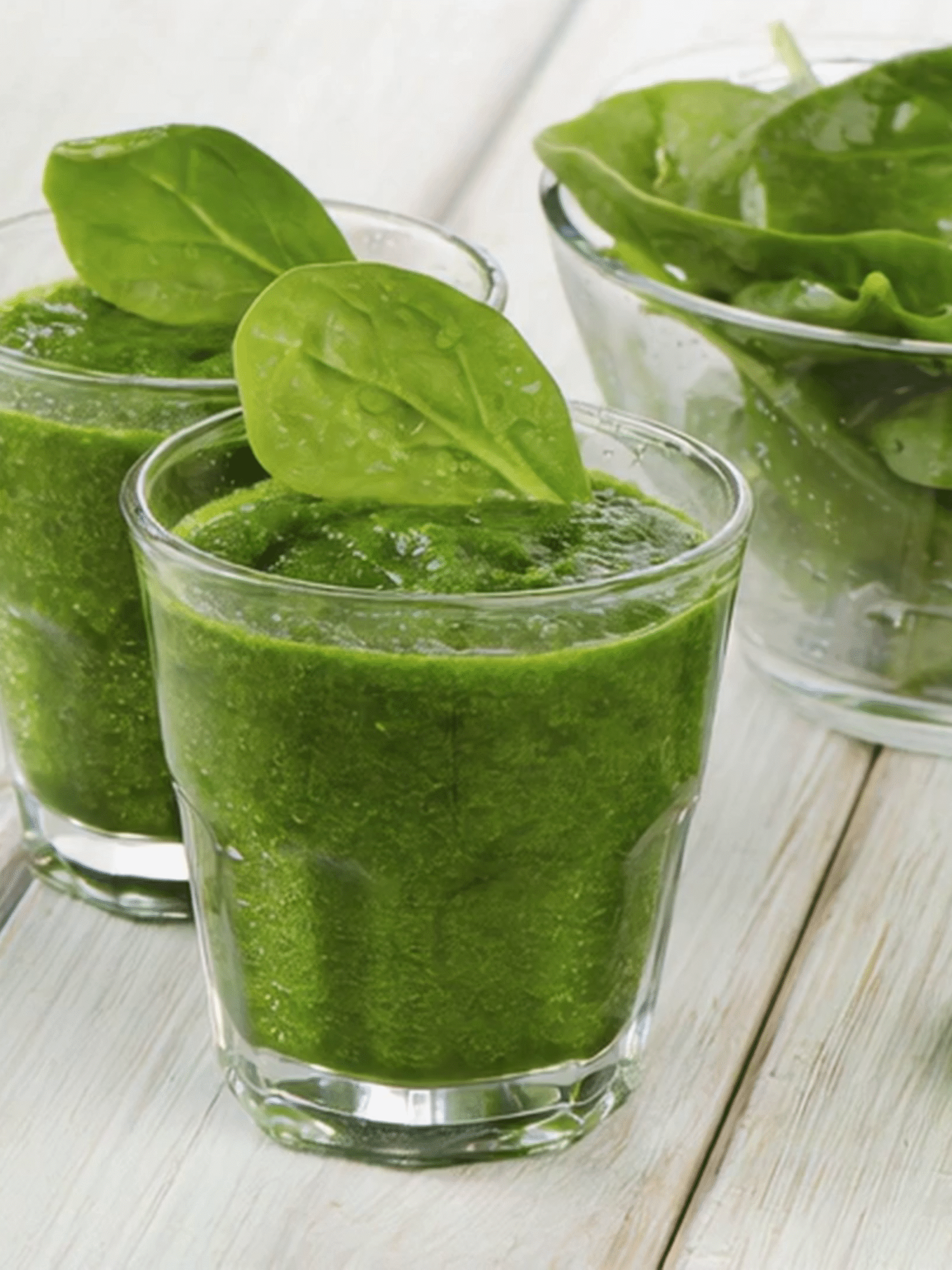 Green Detox Smoothie with Fresh Spinach Two glasses of green detox smoothie garnished with fresh spinach leaves on a white wooden table