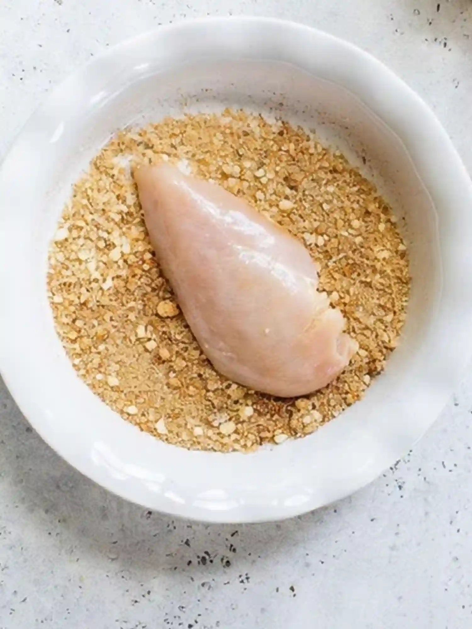 Air Fryer Chicken Breast Breaded Before Cooking Raw chicken breast coated in breadcrumbs in white bowl