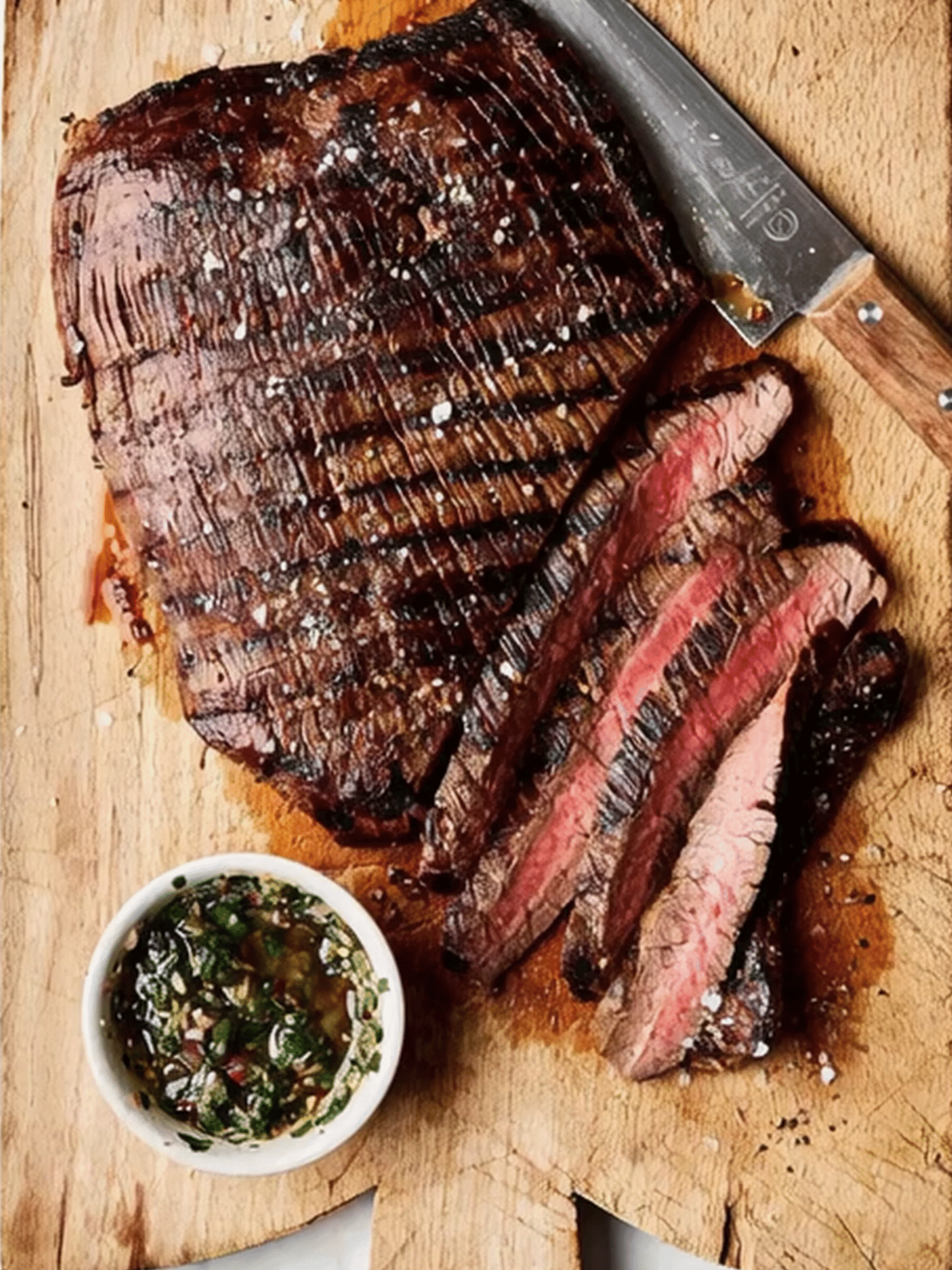Grilled Flank Steak with Pink Salt Barbecue Marinade Grilled flank steak sliced medium rare on a wooden board with pink salt barbecue marinade and herbs