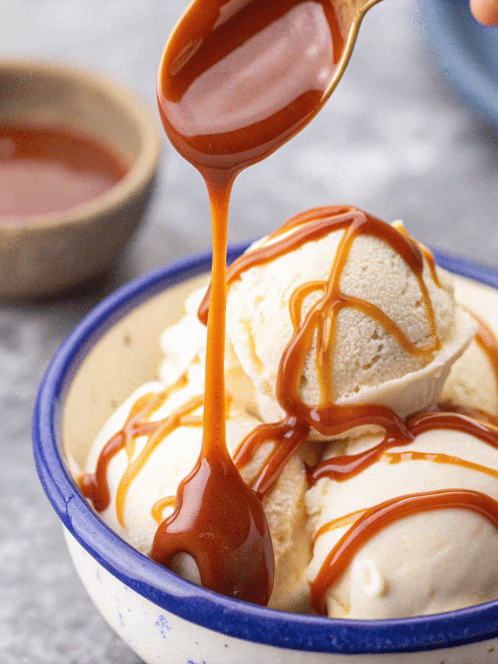 Salted Caramel with Pink Salt on Vanilla Ice Cream Vanilla ice cream scoops drizzled with salted caramel with pink salt from a spoon into a ceramic bowl