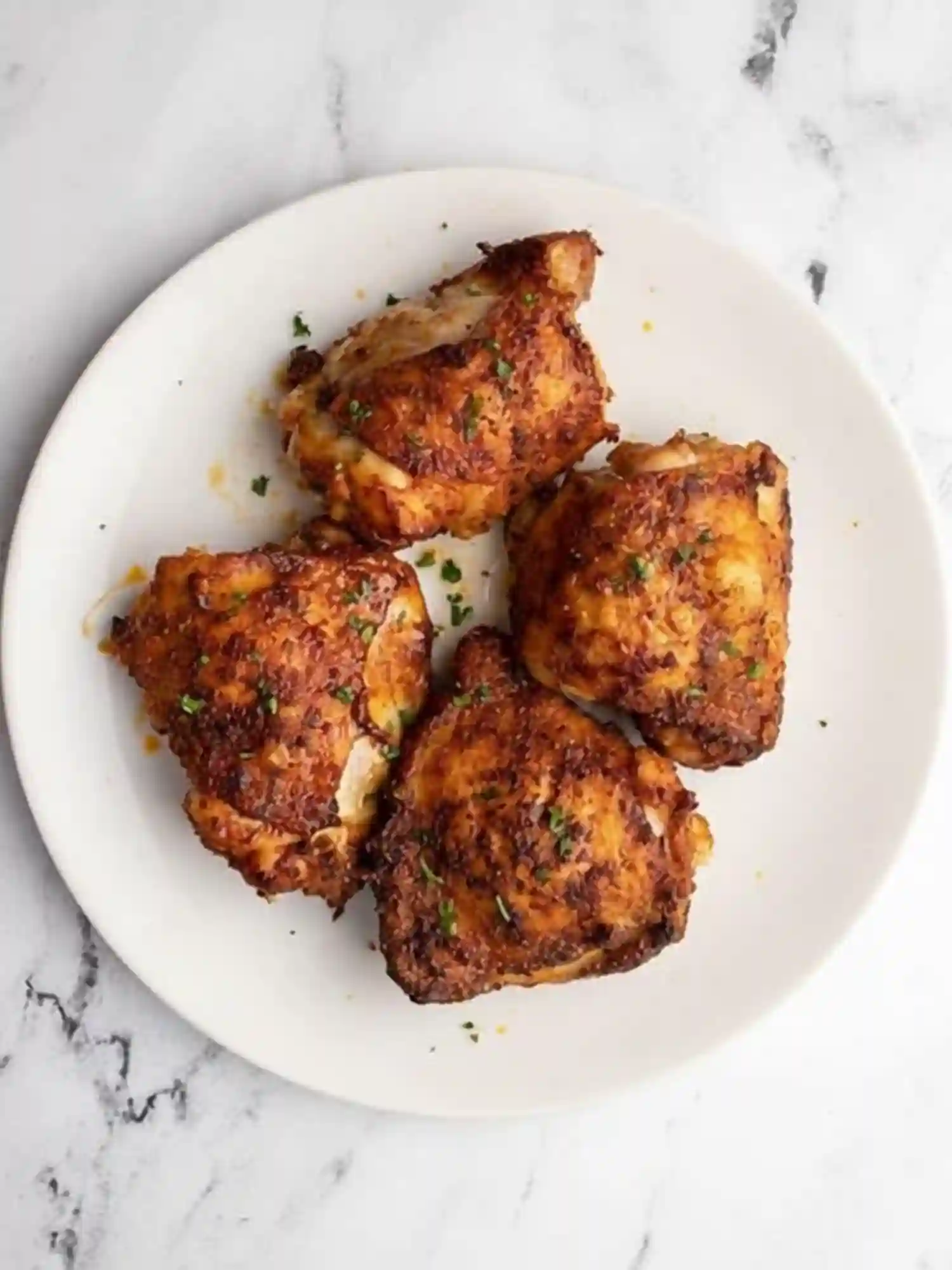 Crispy Air Fryer Chicken Thighs Ready to Serve Crispy golden-brown air fryer chicken thighs served on a white plate with fresh herbs.