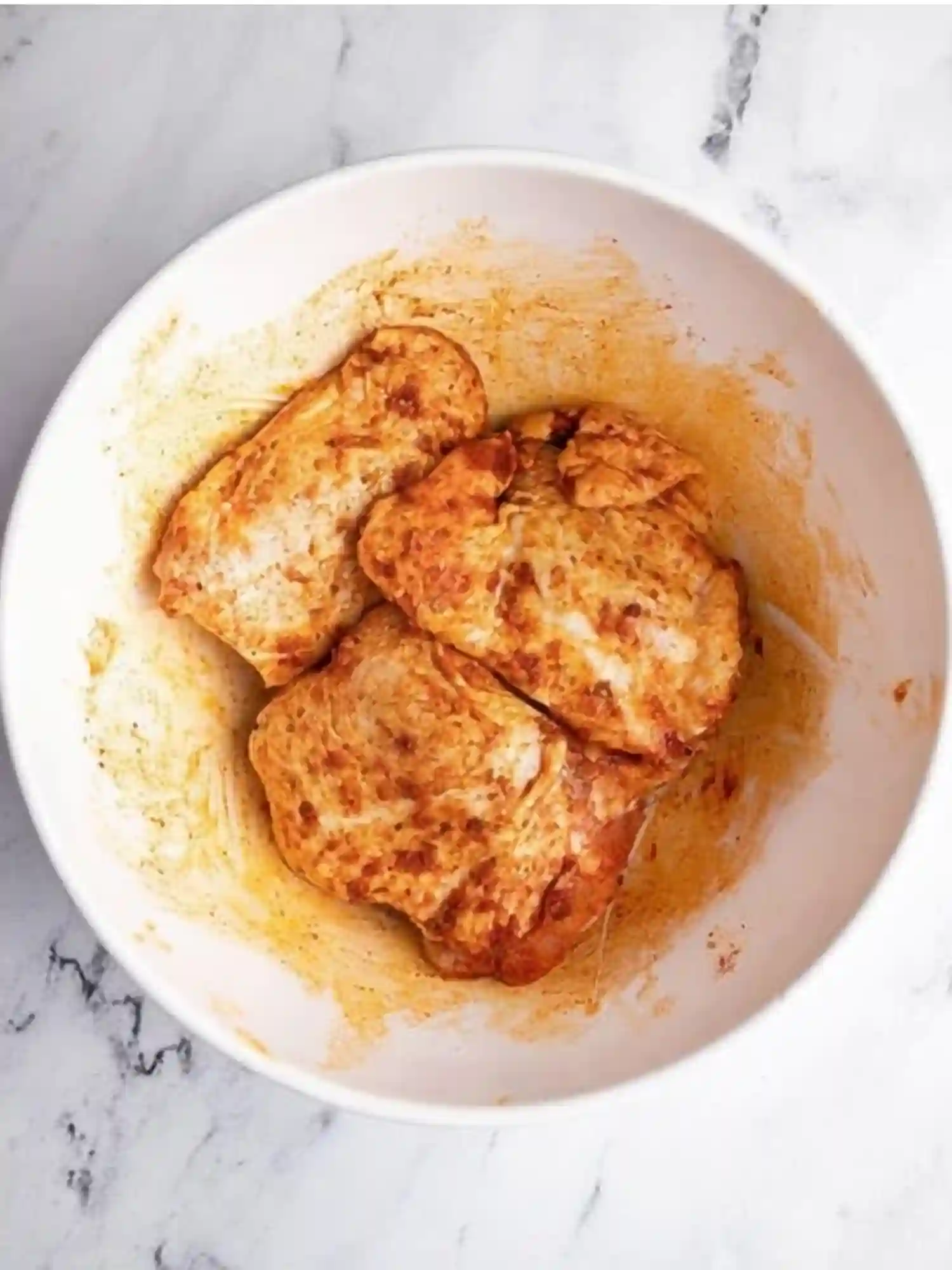 Marinated Chicken Thighs for Air Fryer Recipe Raw chicken thighs marinated with olive oil, paprika, garlic powder, onion powder, and spices in a white mixing bowl.