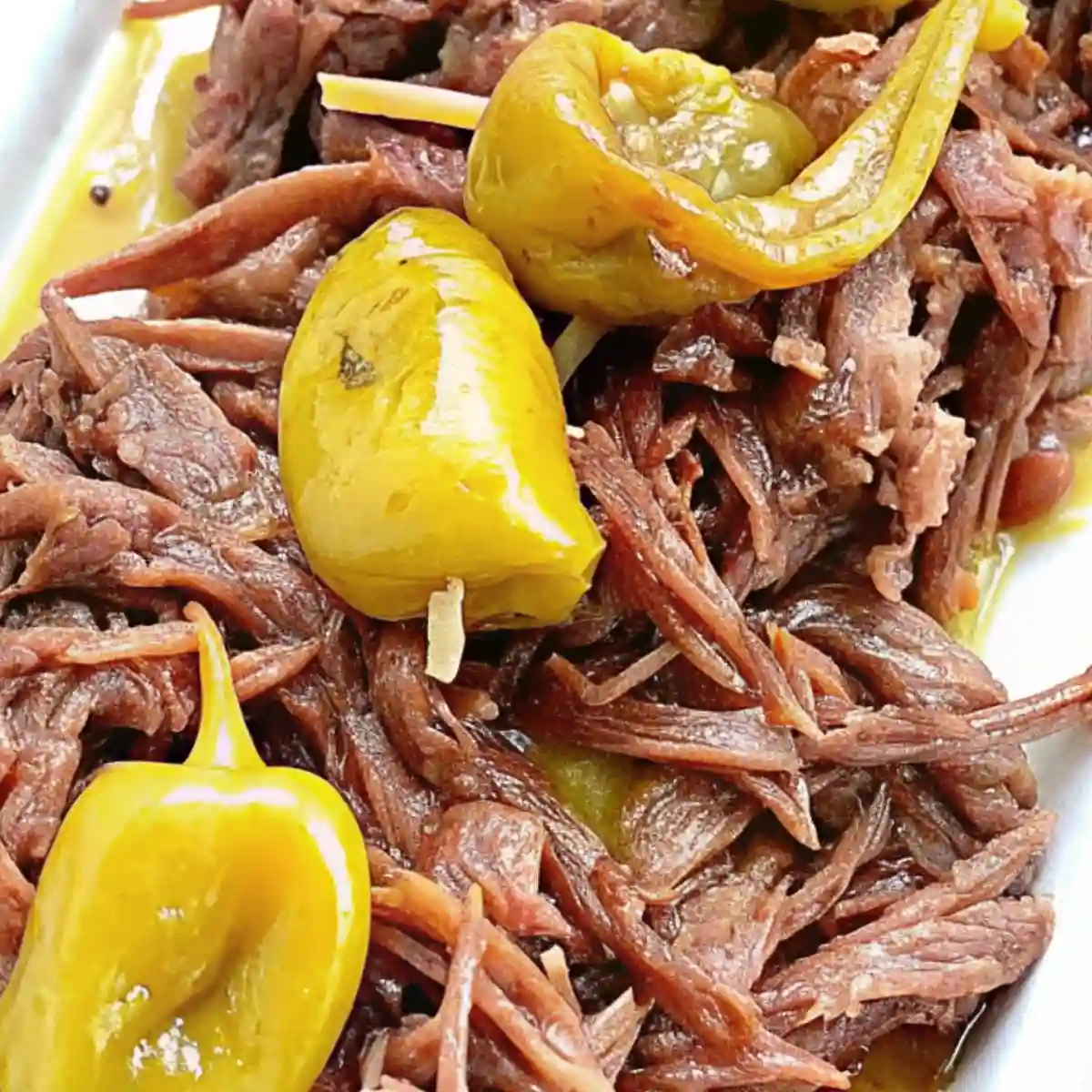 Shredded Mississippi Pot Roast with whole pepperoncini peppers on a white plate