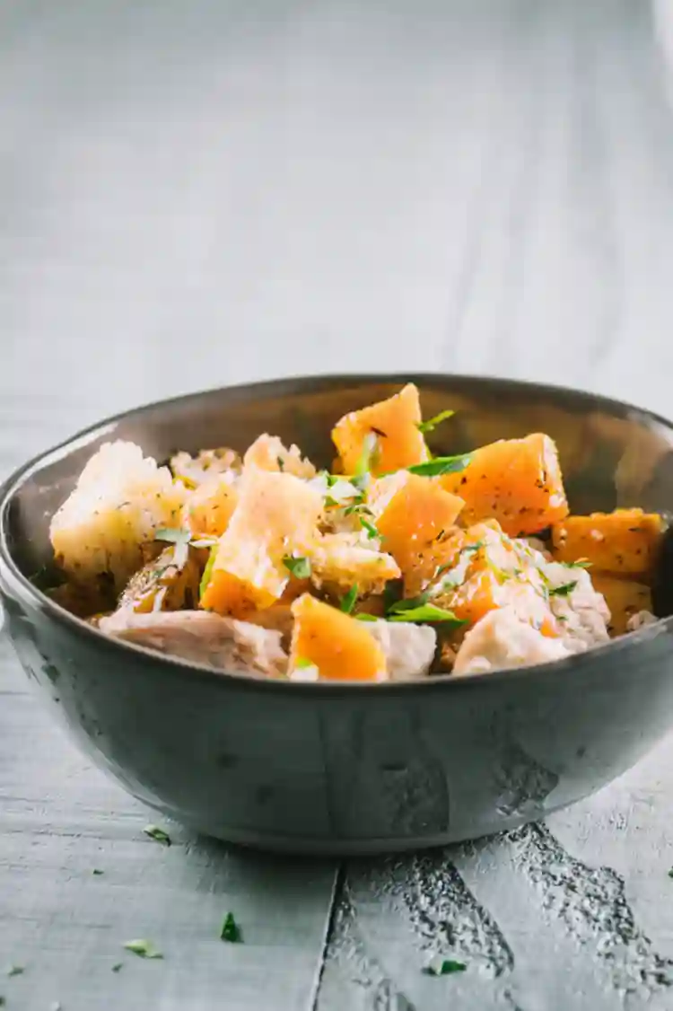 Roasted one pan chicken and butternut squash with croutons in a dark bowl on a wooden table