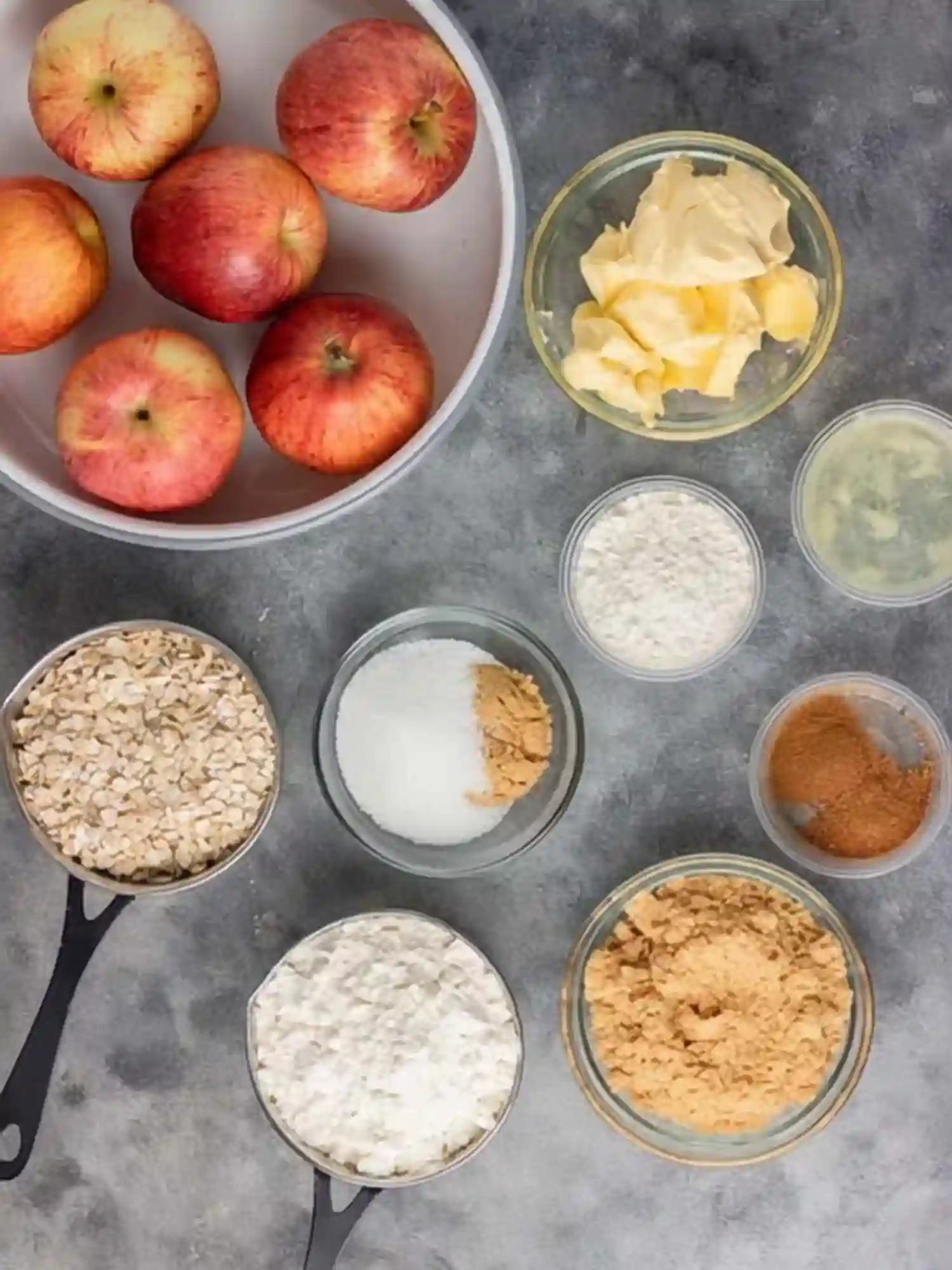 Simple Apple Crumble Apple Crisp Ingredients Preparation Ingredients for Simple Apple Crumble Apple Crisp with apples, butter, oats, flour, sugar, and cinnamon on a gray background