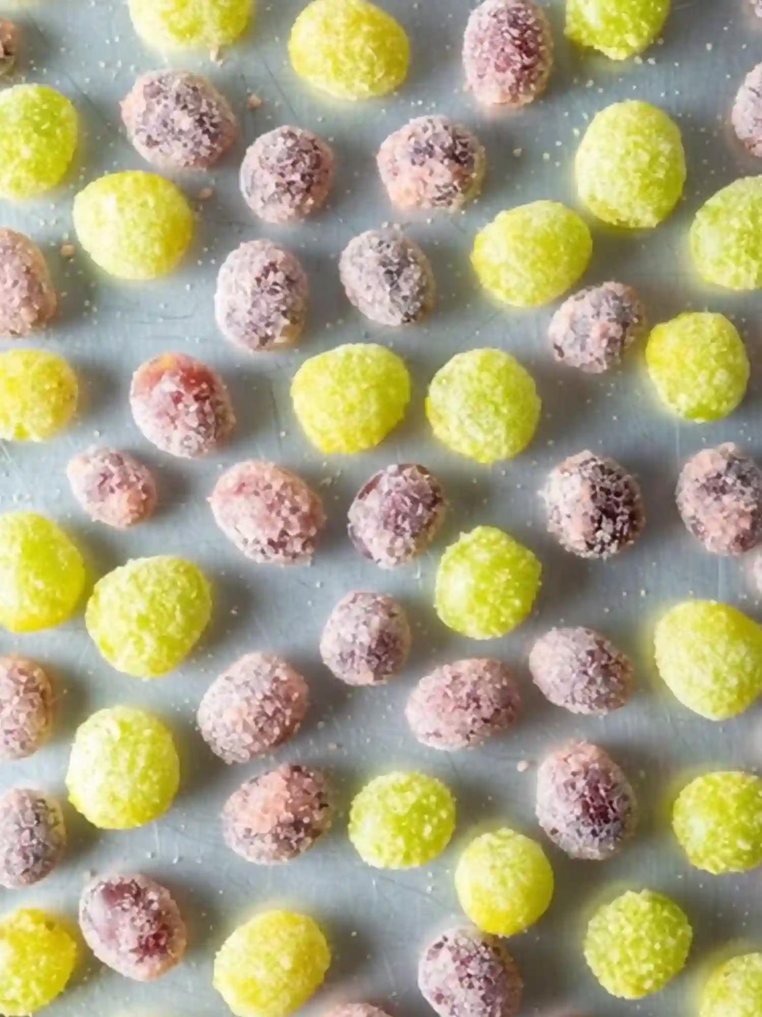 Candied grapes recipe with green and red grapes coated in sugar, neatly arranged on a tray and ready to dry for a crunchy candy finish.