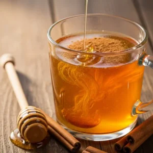 Glass mug of the Cinnamon and Honey Fat Burning Mix with honey drizzling into warm water and cinnamon swirling inside, surrounded by cinnamon sticks and a honey dipper.