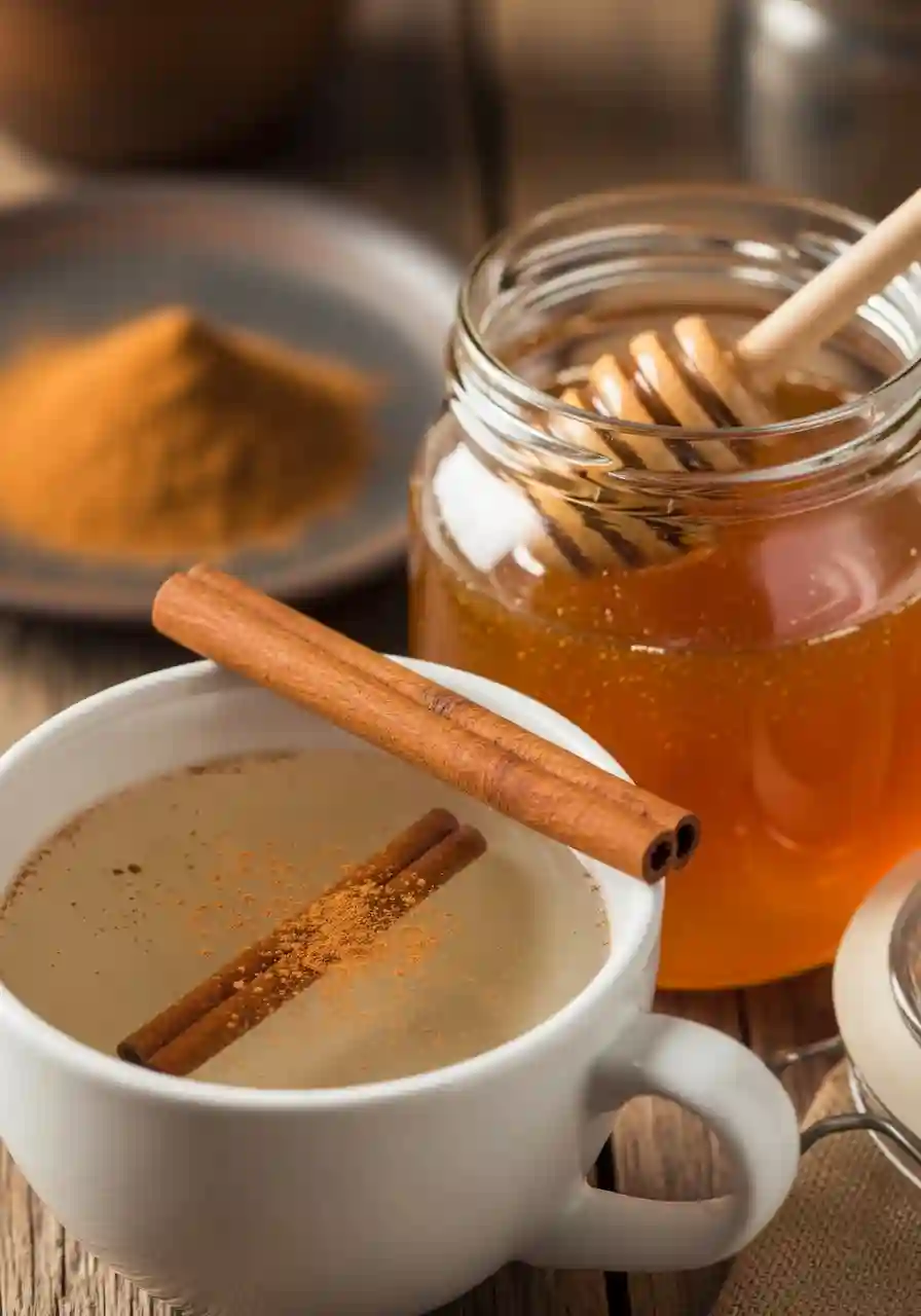 Honey Trick for Weight Loss cinnamon and honey fat-burning drink in a white cup beside a jar of raw honey and cinnamon sticks on a wooden table.