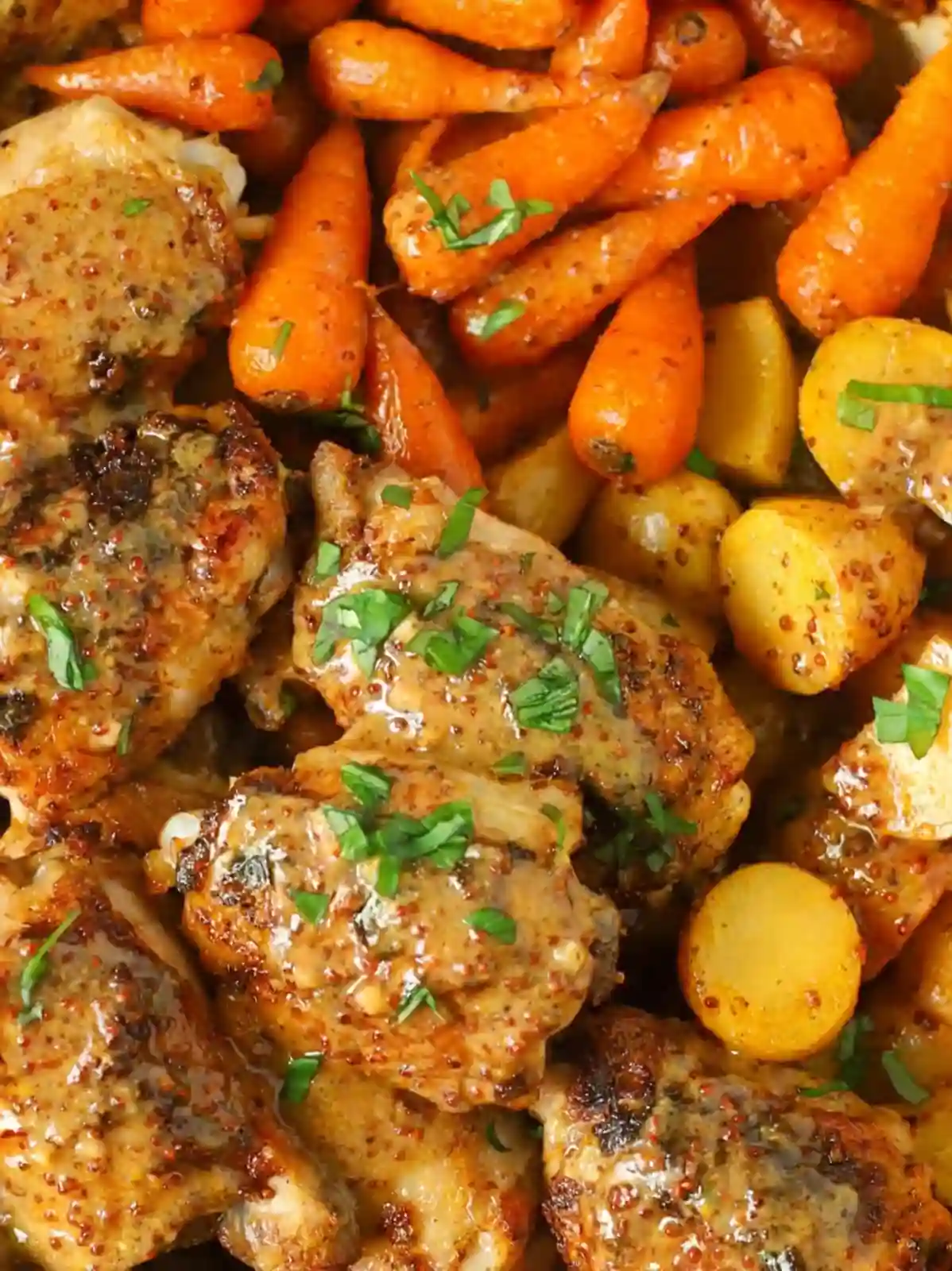 Close-up of honey mustard chicken thighs with roasted carrots and baby potatoes in a one pan dinner