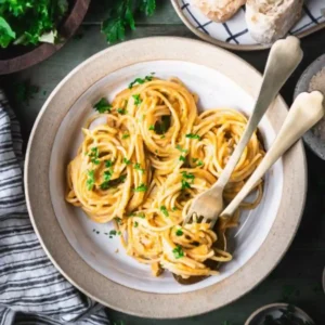 Creamy pumpkin chicken pasta served in a rustic white bowl, topped with fresh chopped parsley and twirled spaghetti, surrounded by bread and salad.