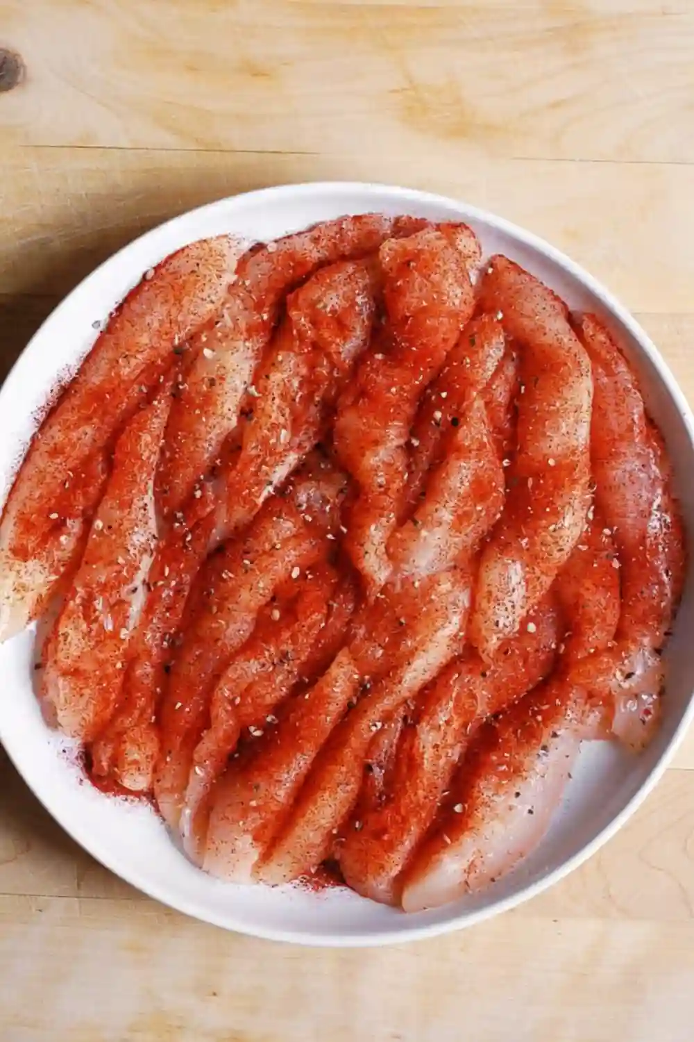 Raw chicken tenderloins seasoned with paprika, salt, and pepper in a white bowl
