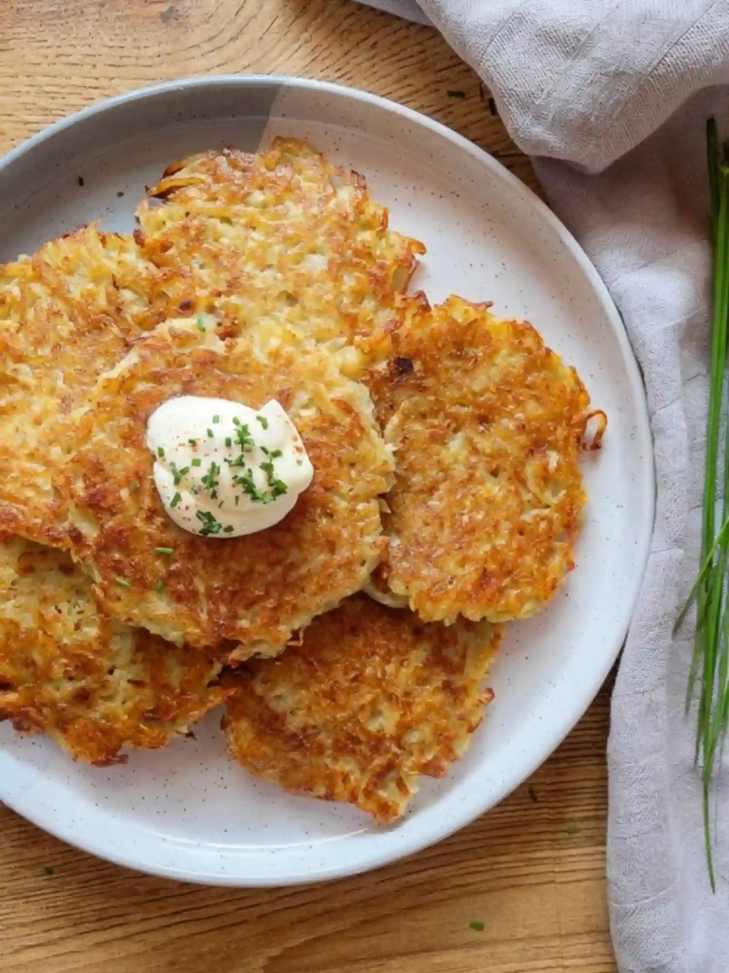 Crispy German Potato Pancakes Served with Sour Cream Top view of crispy German potato pancakes on a white plate with sour cream and chives