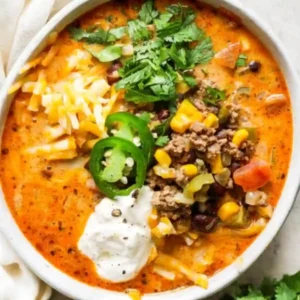 Bowl of creamy taco soup topped with ground beef, corn, black beans, shredded cheese, jalapeño slices, sour cream, and fresh cilantro.