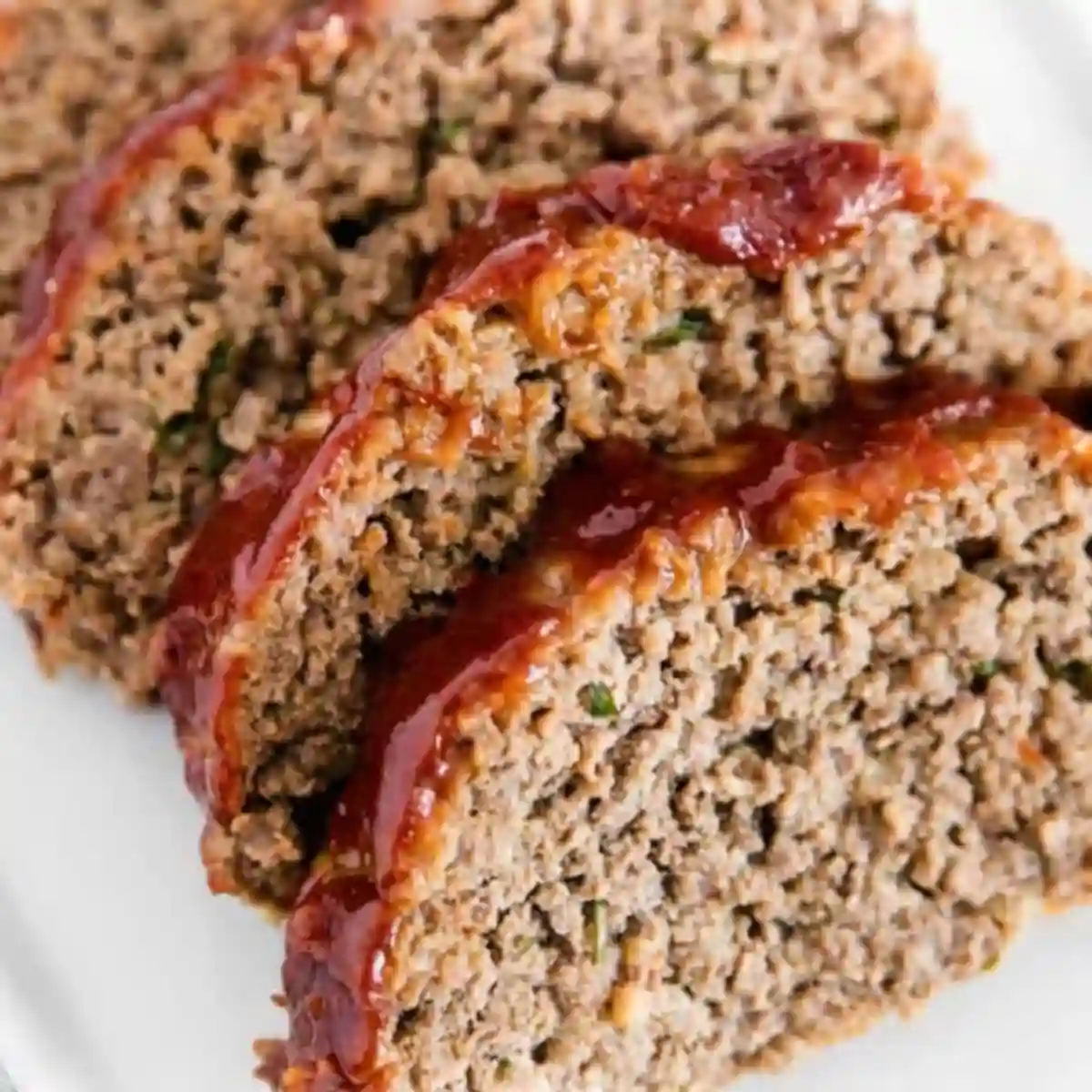 Three slices from classic meatloaf recipes, juicy and glazed with ketchup, served on a white plate