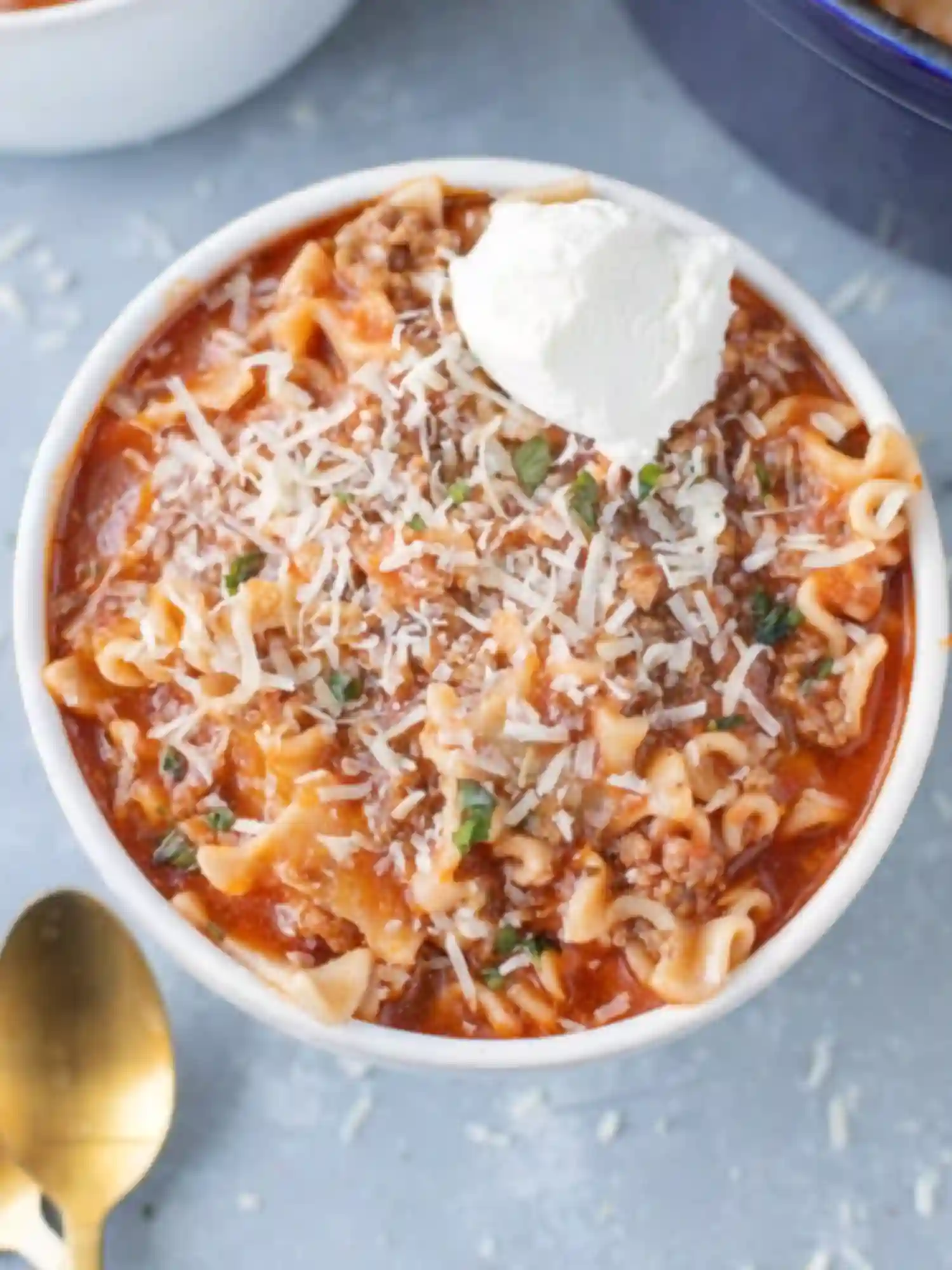 Bowl of High Protein Lasagna Soup topped with ricotta, parmesan, and fresh basil on a light blue background