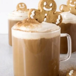 A festive mug of coffee from a homemade Gingerbread Latte Recipe, topped with whipped cream and a gingerbread man cookie.