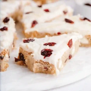 Cranberry bliss bars recipe with cream cheese frosting and dried cranberries, sliced into triangles on parchment paper