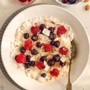 High protein breakfast cottage cheese bowl topped with raspberries, blueberries, coconut flakes, and almonds in a white bowl