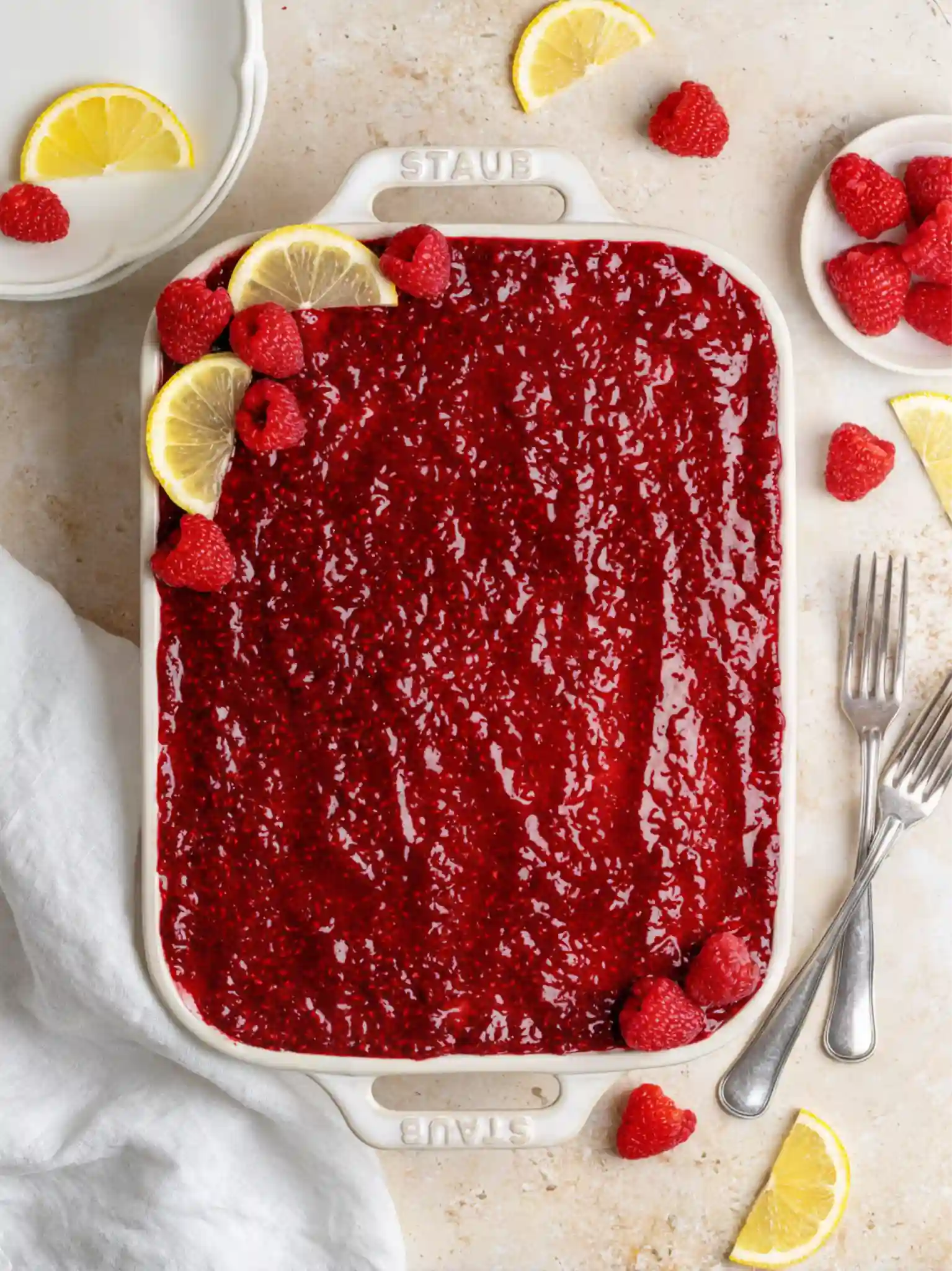 Overhead view of a whole Fresh Raspberry Tiramisu in a white ceramic dish, topped with raspberry jam and garnished with fresh raspberries and lemon slices