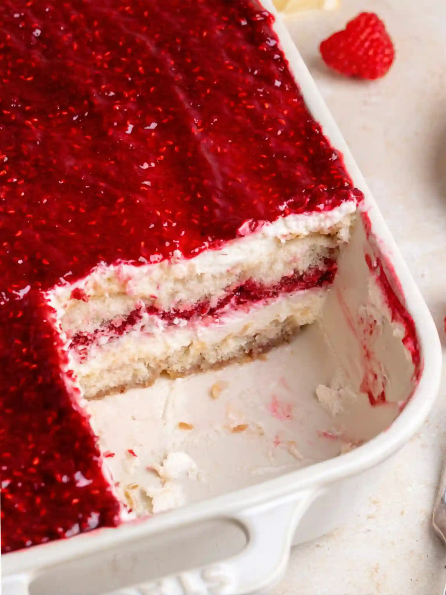 Close-up of sliced Fresh Raspberry Tiramisu in a white baking dish, showing layers of mascarpone cream, raspberry jam, and soaked ladyfingers