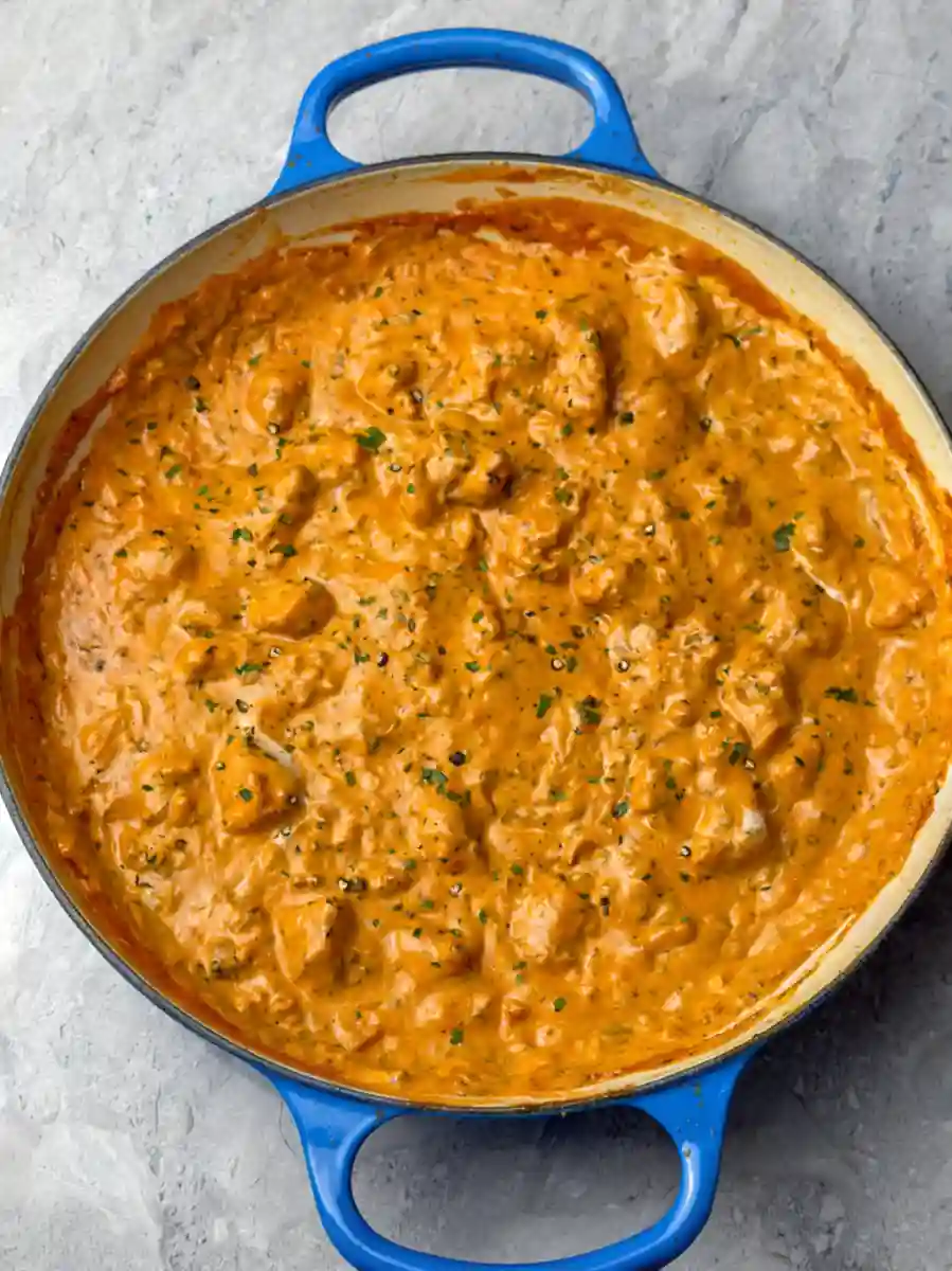Butter Chicken simmering in a creamy orange sauce in a large blue pan