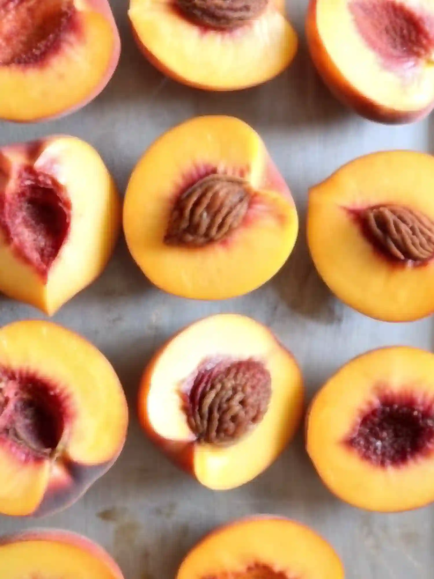 Halved ripe peaches with visible pits arranged on a baking sheet, showcasing their vibrant color and fresh texture for peach dessert preparation