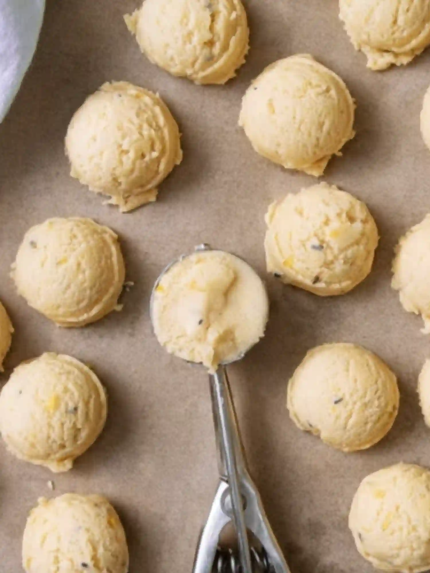 Scoops of lemon lavender cookie dough arranged on parchment paper with a metal cookie scoop.