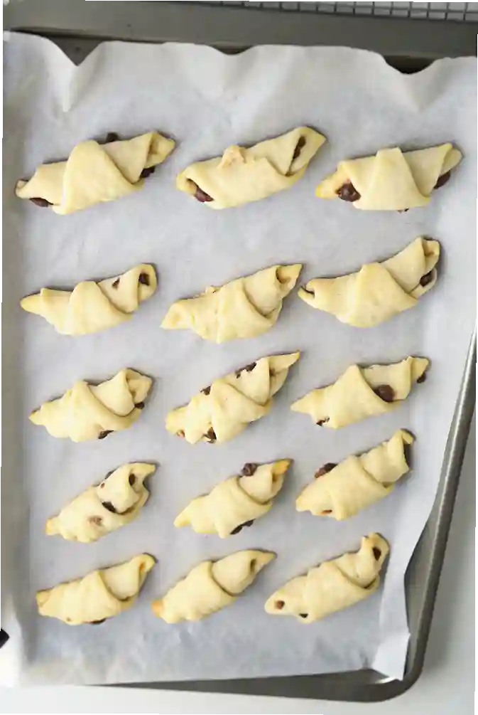 Rolled crescent dough filled with chocolate and marshmallows arranged on a parchment-lined baking tray, ready for the oven