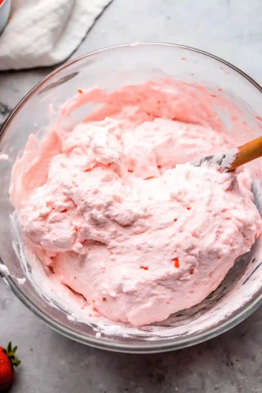 Mixing cottage cheese jello salad in a glass bowl with strawberry gelatin and whipped topping being folded together.