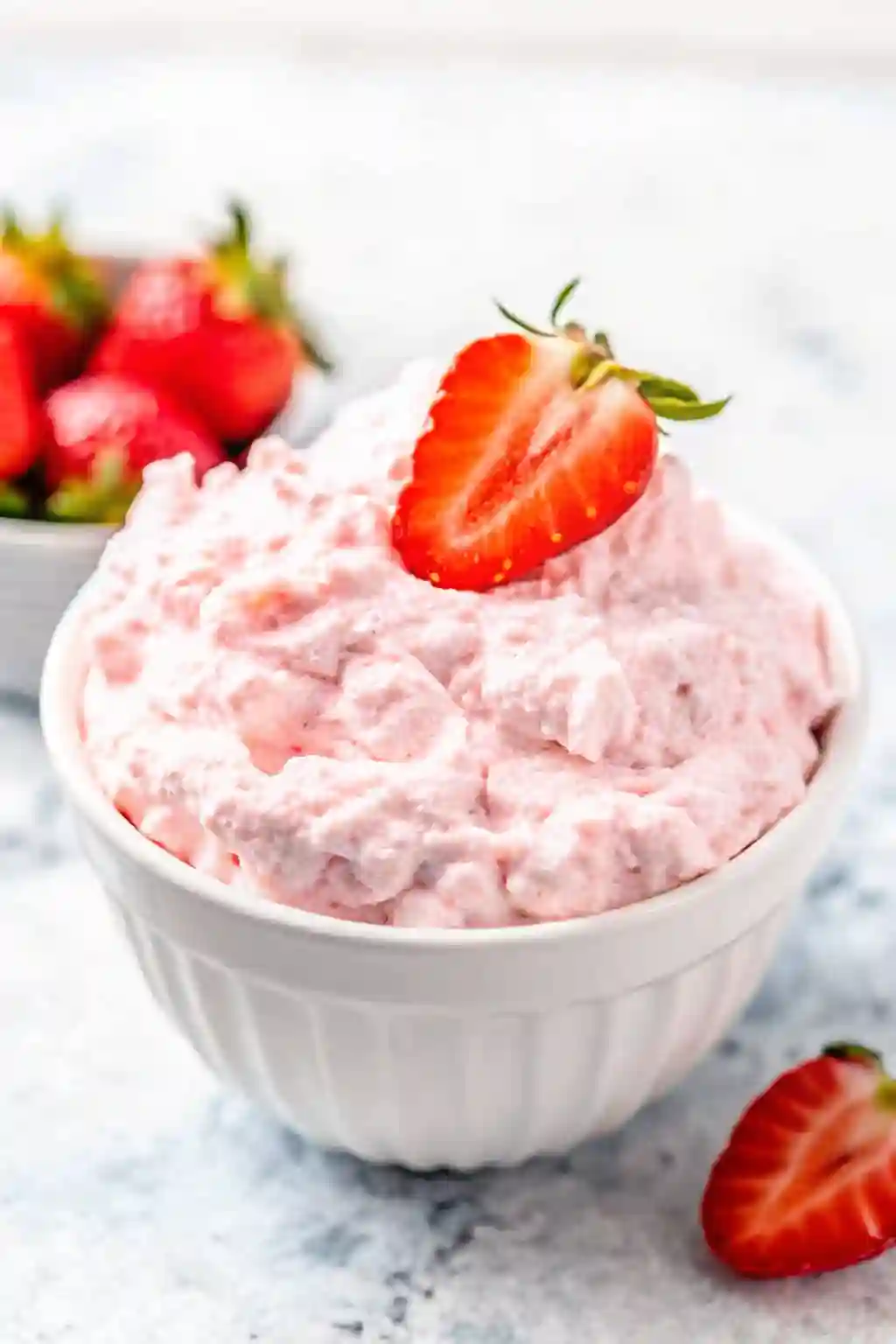 Strawberry cottage cheese jello salad served in a white bowl and topped with a fresh strawberry on a marble surface.