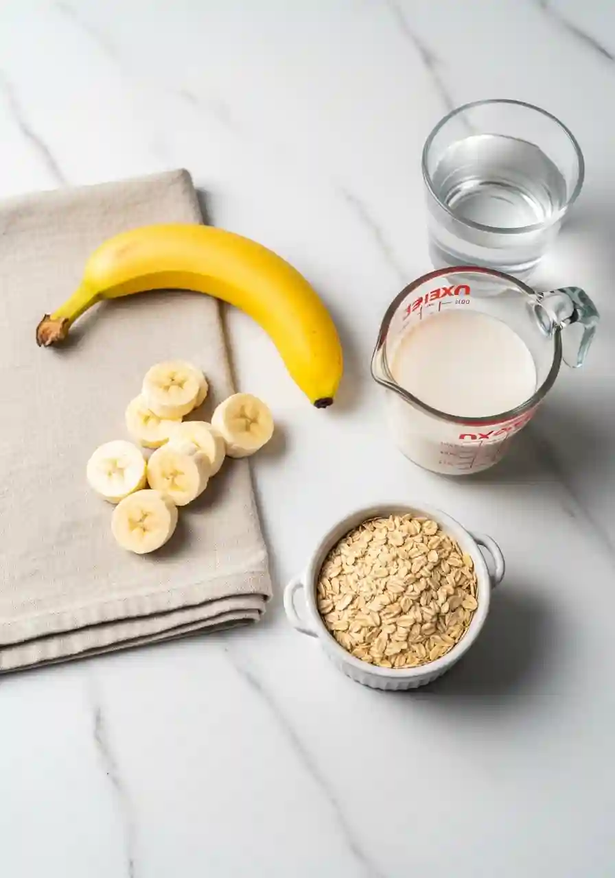 Ingredients for oats smoothie for weight loss including rolled oats, banana, almond milk, and water on a marble surface