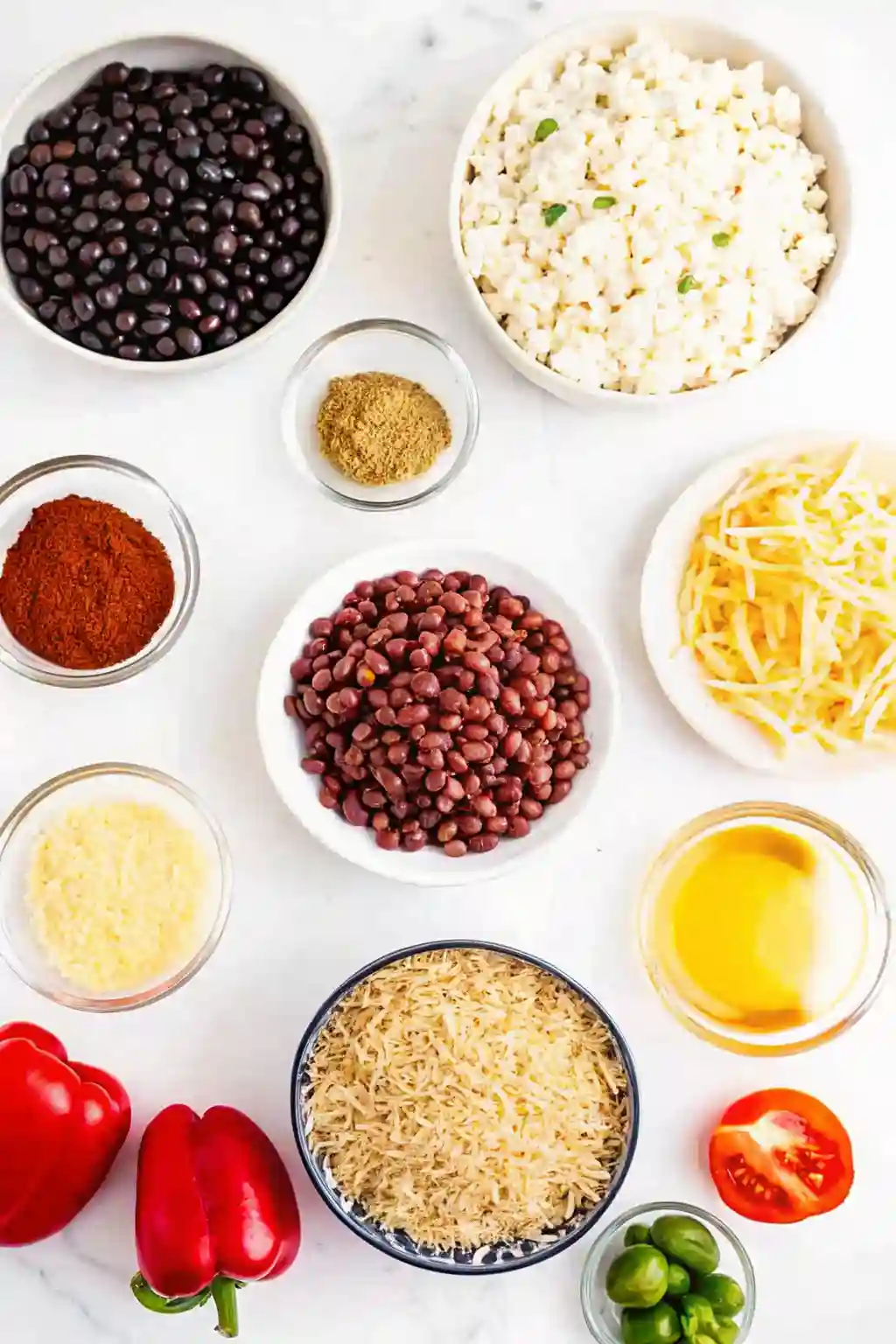 Chicken burrito casserole ingredients including black beans, shredded chicken, rice, cheese, peppers, and spices on a white surface