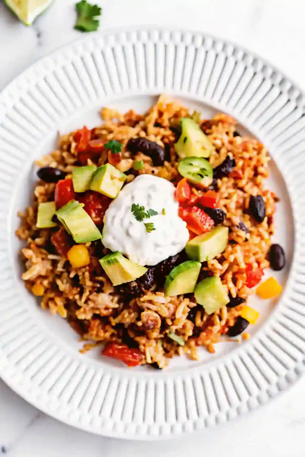 Chicken burrito casserole served with avocado, sour cream, black beans, rice, and vegetables on a white plate