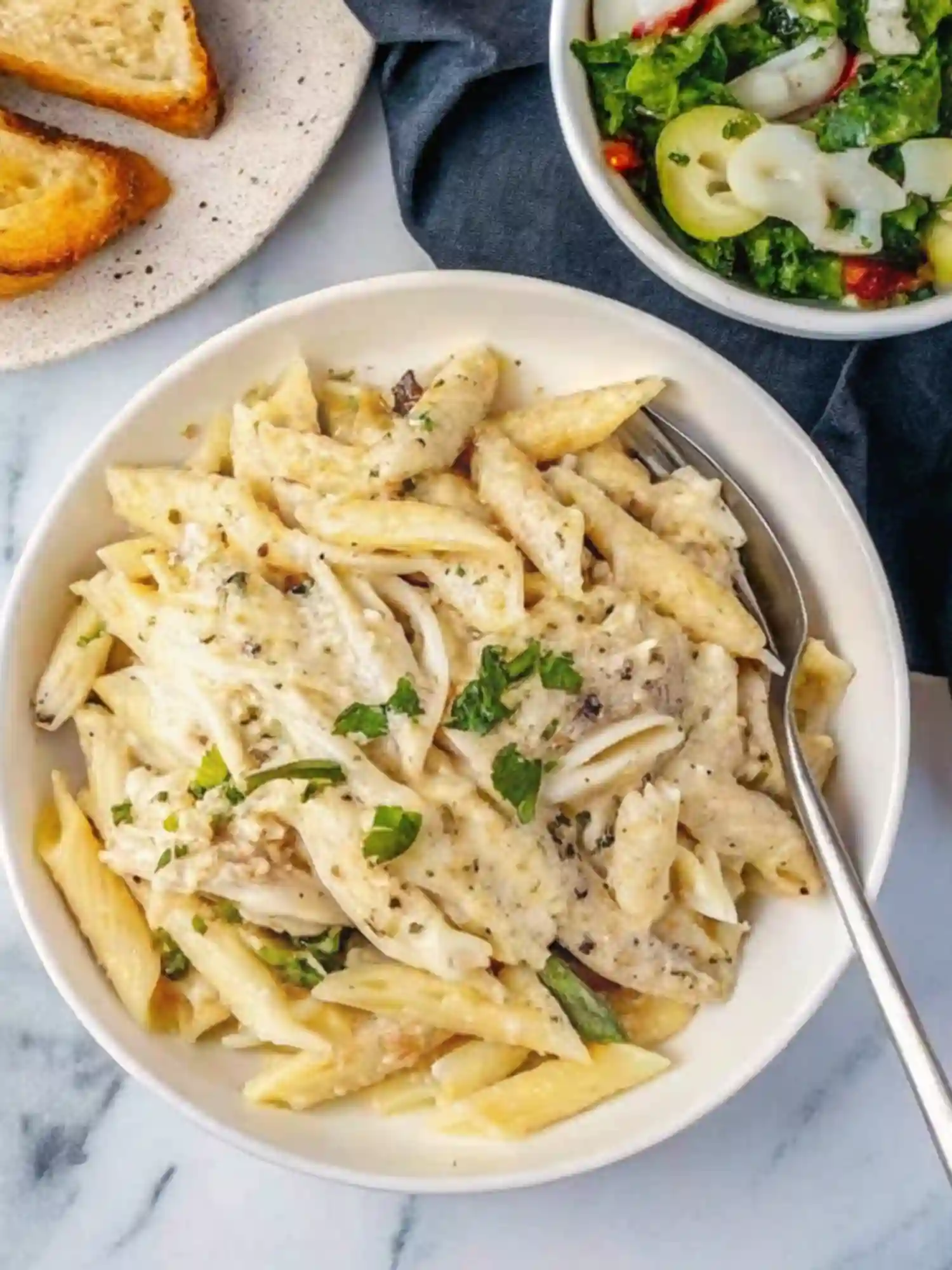 Crockpot chicken alfredo recipe served in a bowl with creamy pasta, shredded chicken, garlic bread, and fresh salad