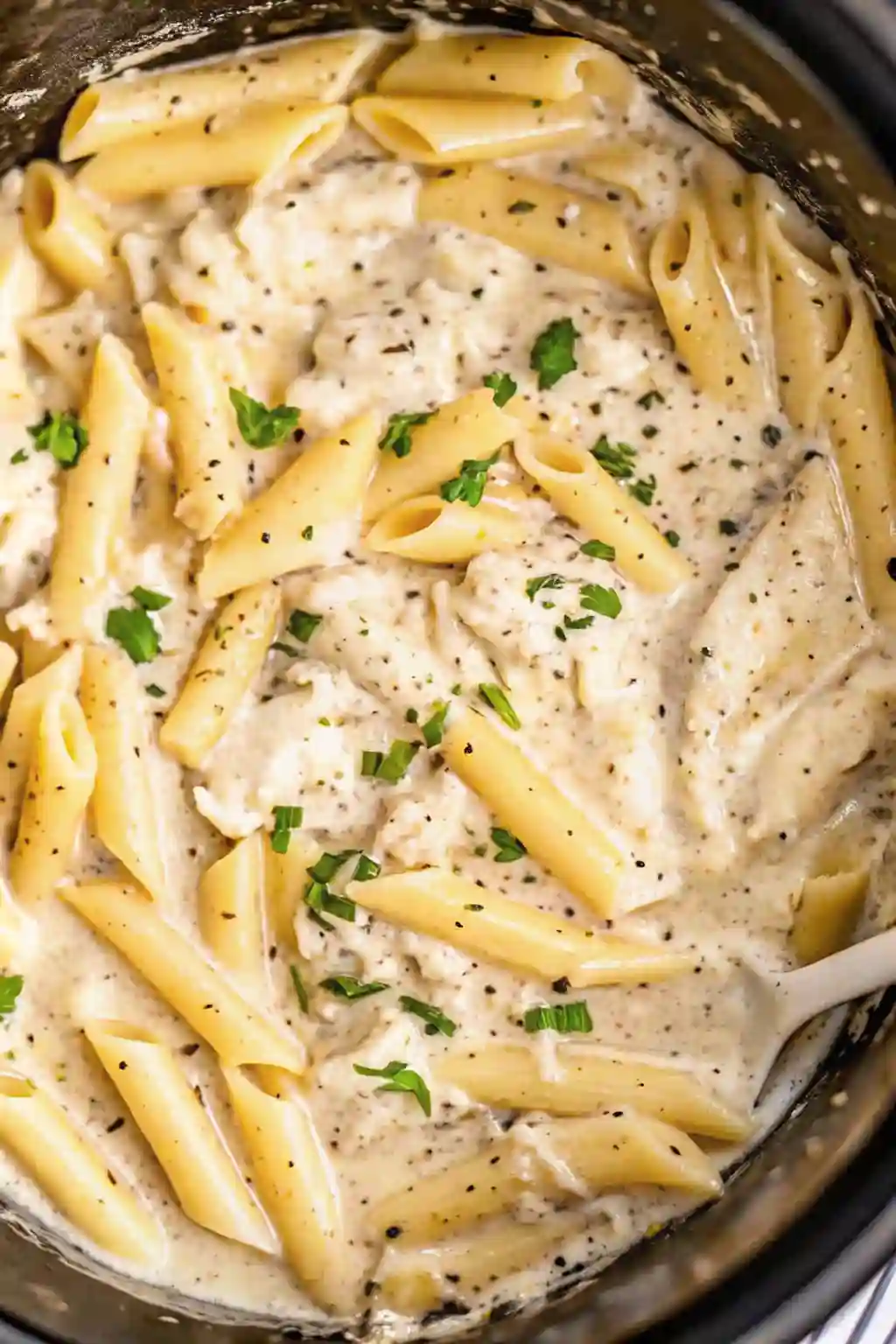 Crockpot chicken alfredo recipe cooking in slow cooker with penne pasta and creamy alfredo sauce