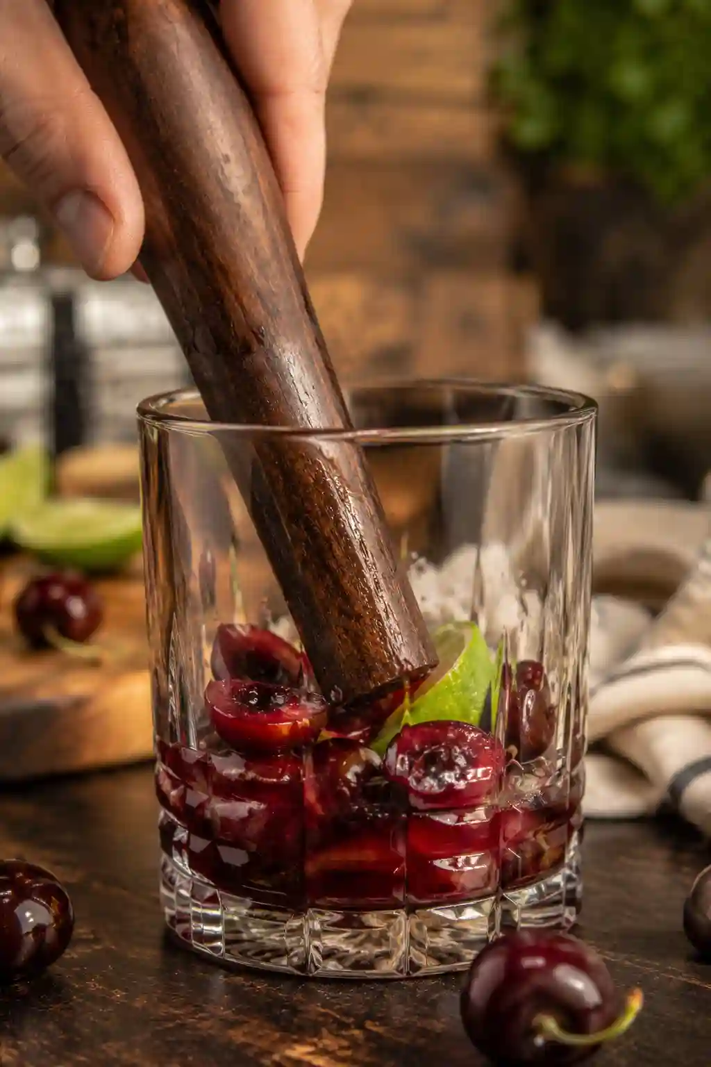 Muddling fresh cherries and lime wedges in a rocks glass to prepare a Tart Cherry Bomb Drink