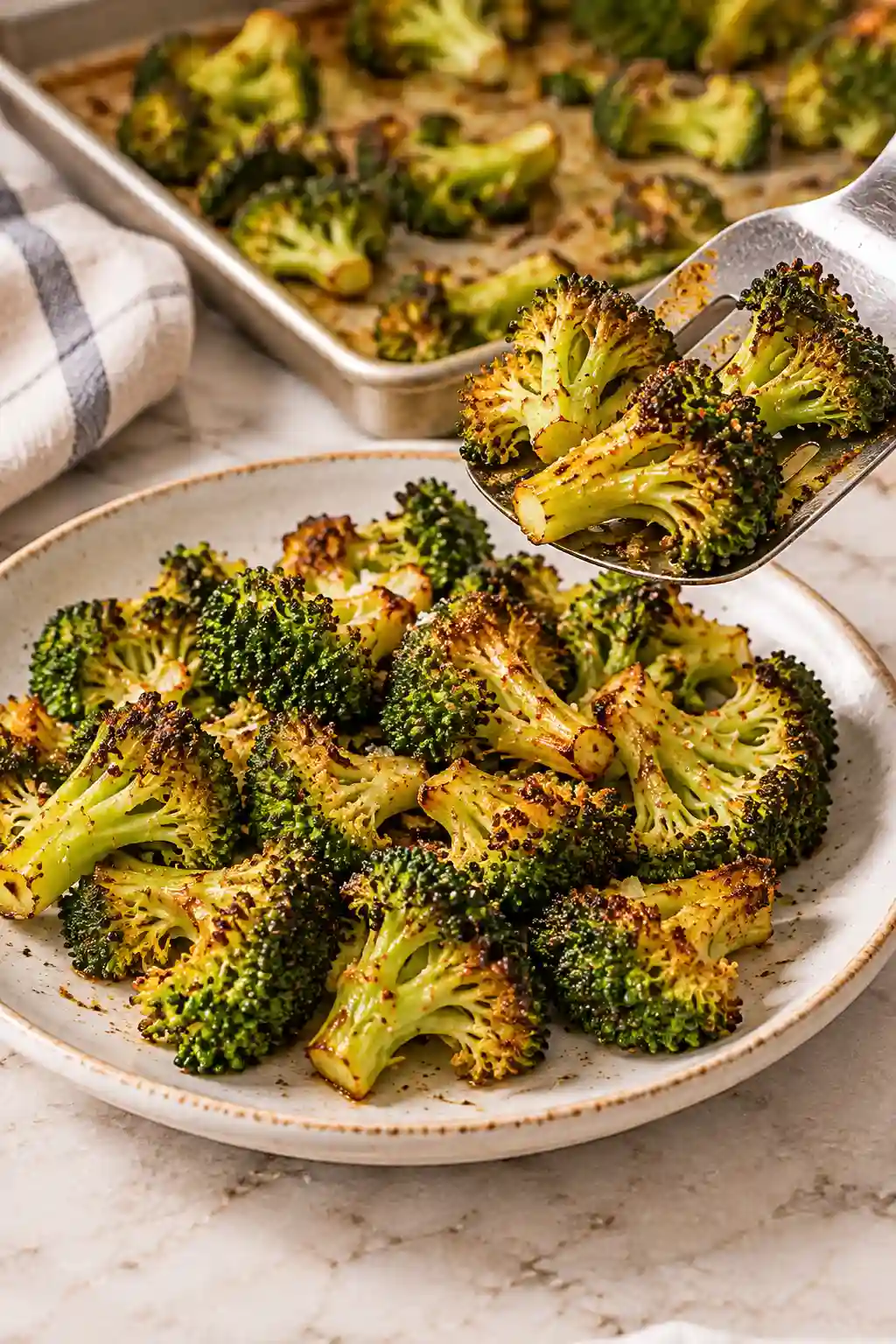 Crispy roasted broccoli being served from a baking sheet onto a plate